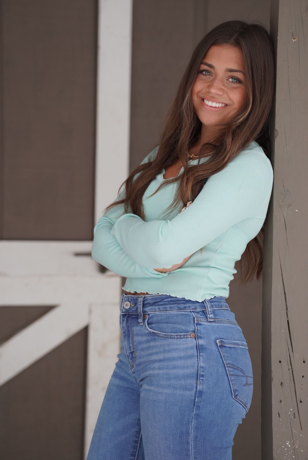 A person in a mint green sweater and blue jeans poses casually against a white wall in a series of photos.