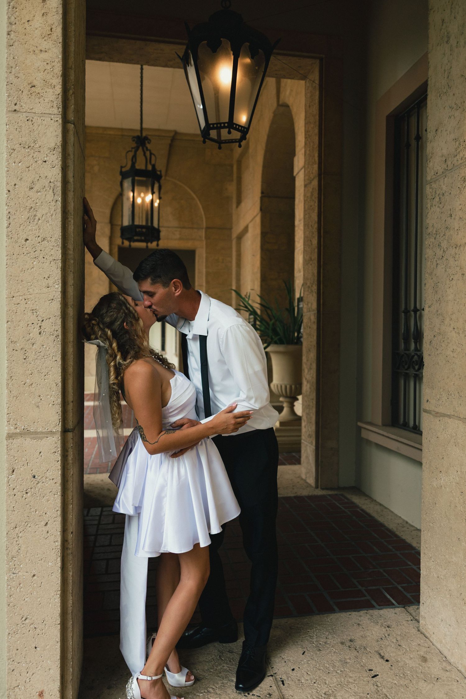 Couple sharing passionate kiss in elegant stone archway with vintage lanterns during wedding day.