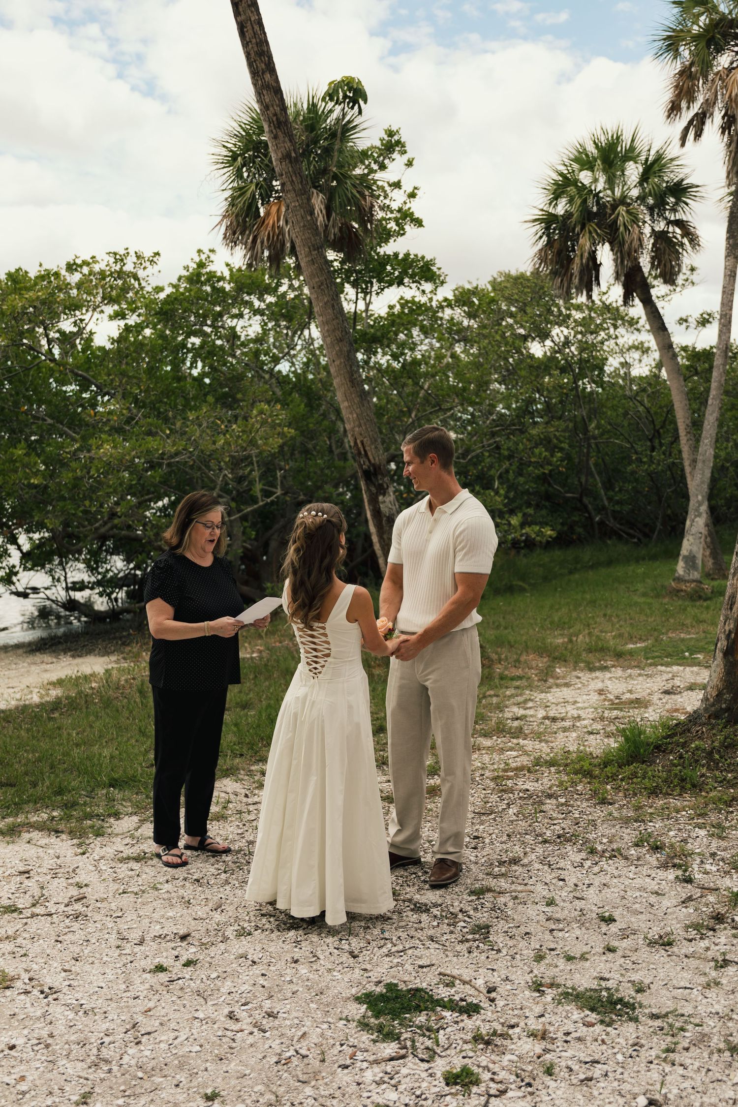 Bride and groom holding hands during intimate outdoor elopement ceremony with officiant near palm trees.
