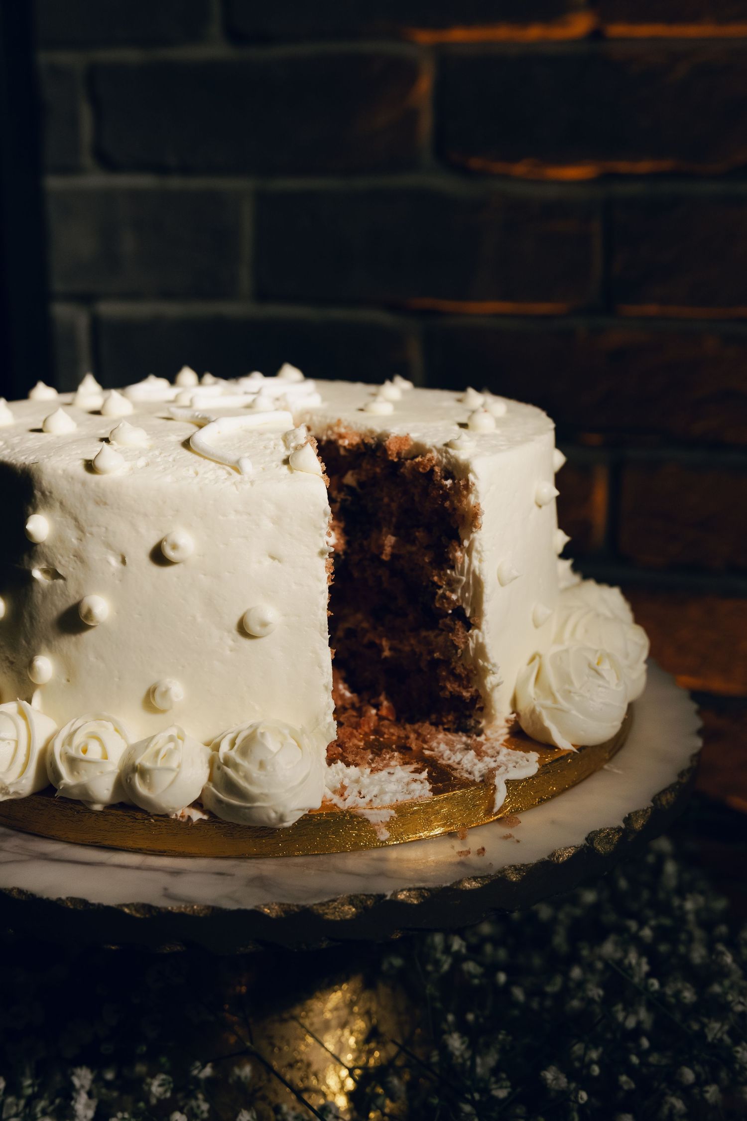 Elegant white wedding cake with rosette frosting and a slice removed on a marble stand.