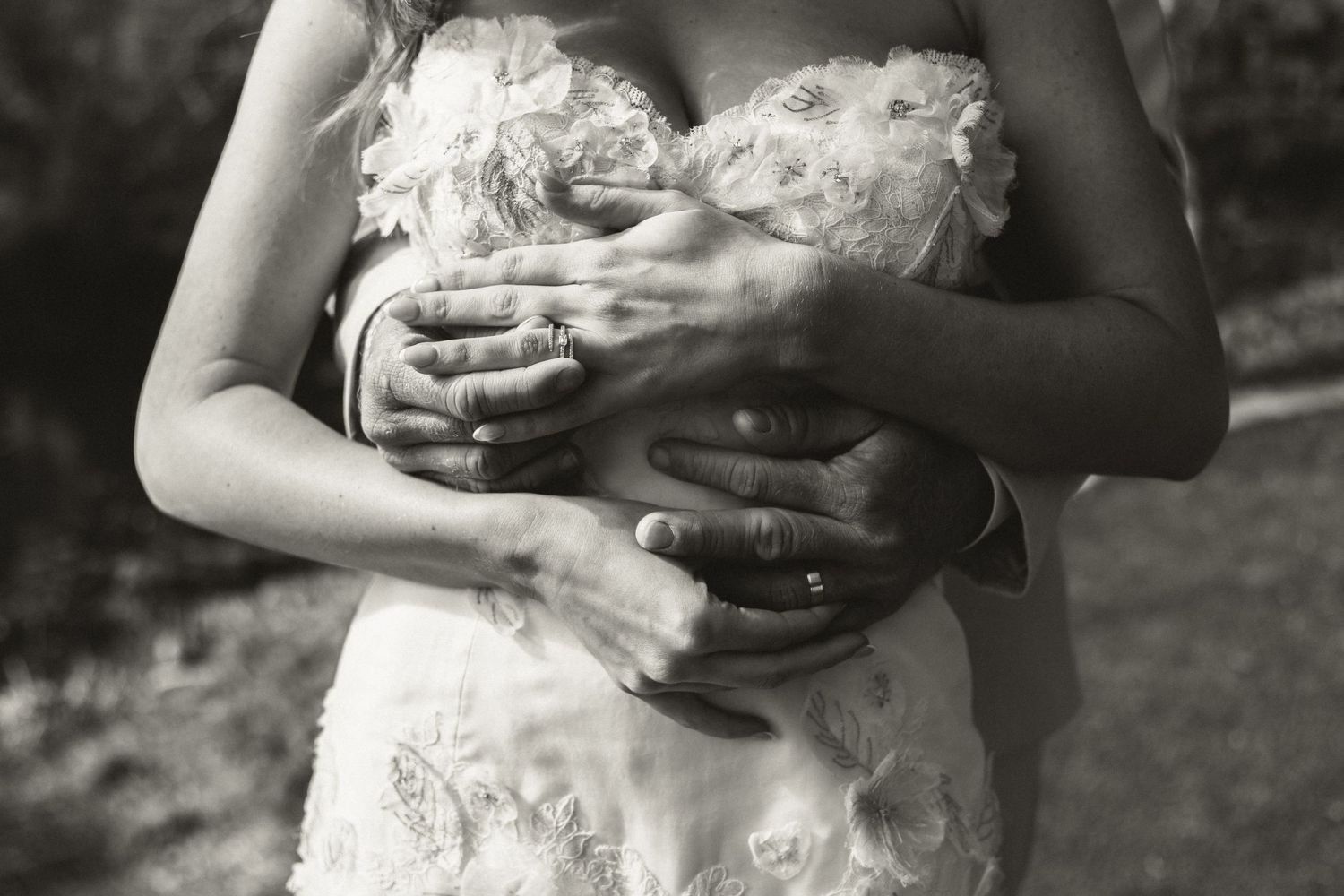 Black and white close-up of bride and groom embracing, showing wedding rings.