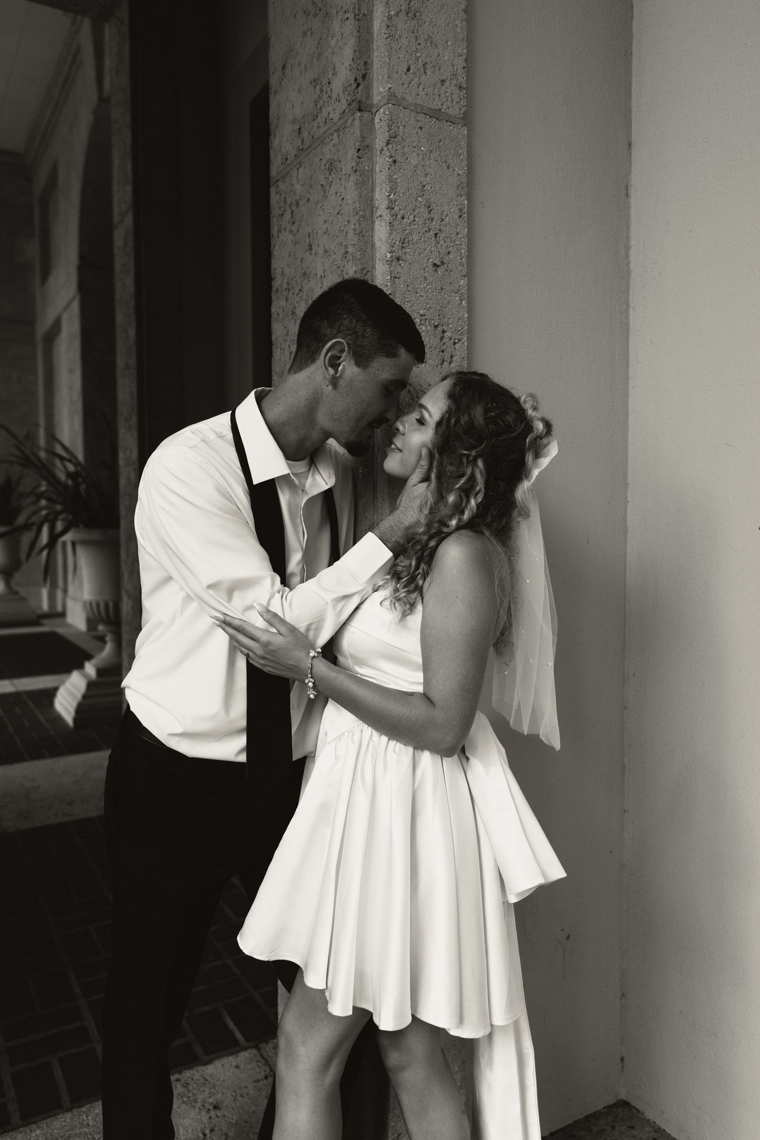 Black and white romantic portrait of newlyweds embracing tenderly in classic architectural corridor.