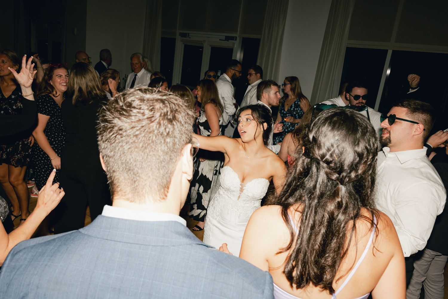 Bride in lace wedding gown dancing joyfully with guests at wedding reception.