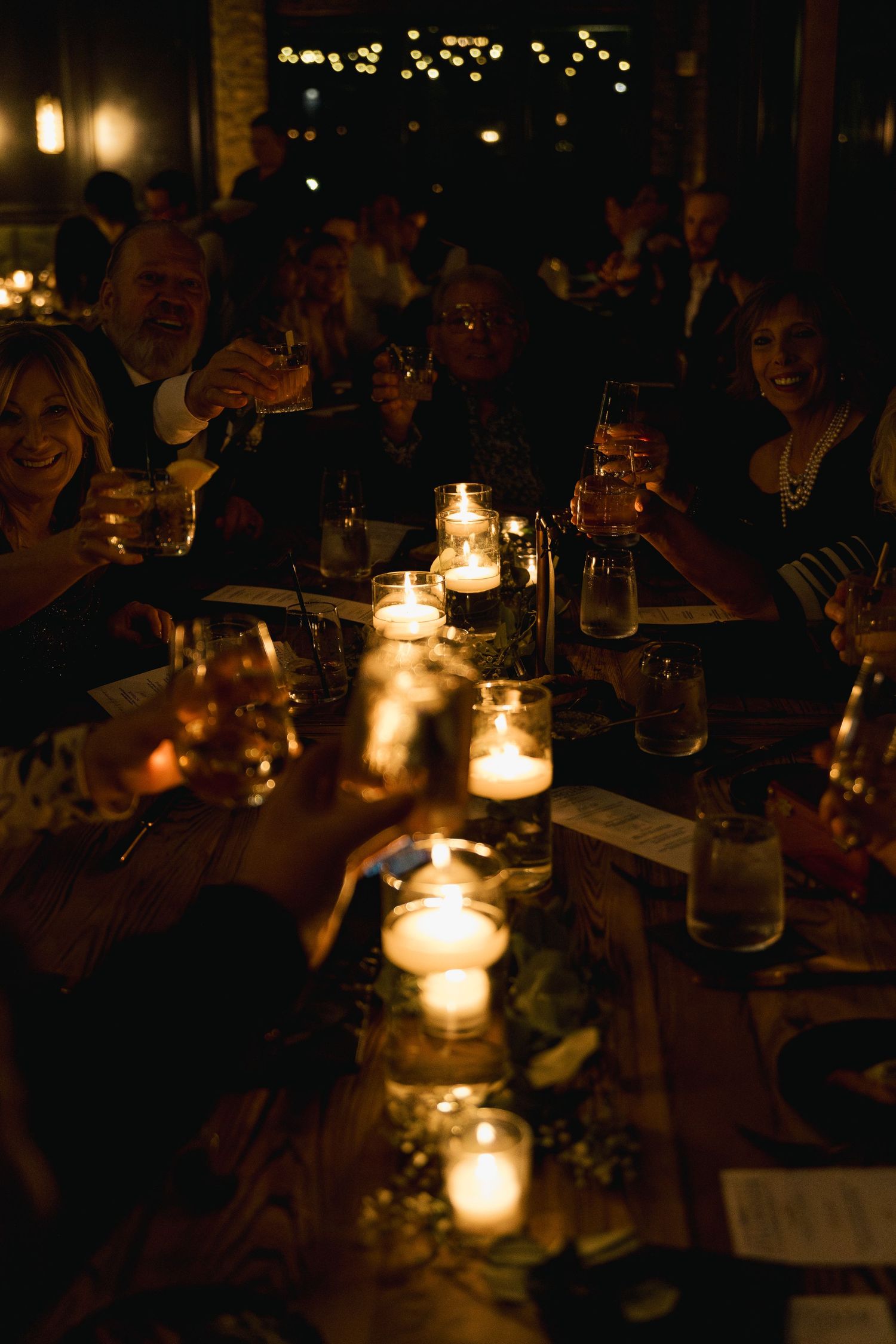 Wedding guests raising glasses in a candlelit toast at a romantic dinner reception.