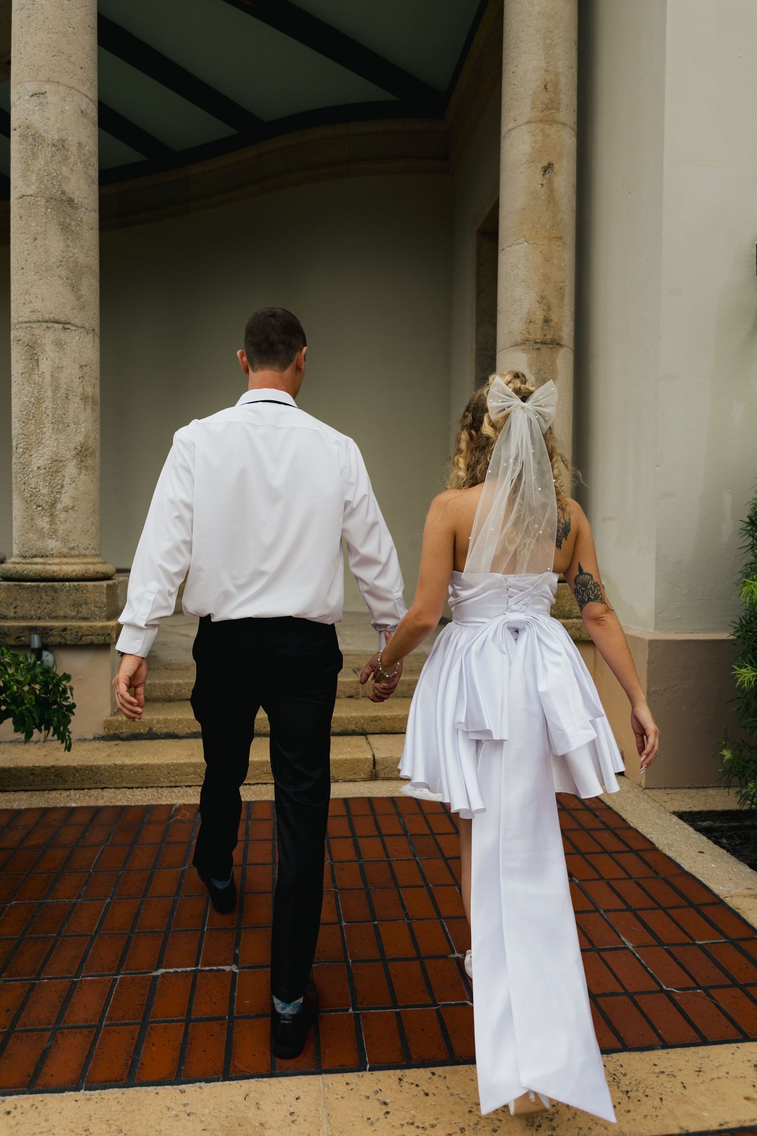 Bride and groom walking hand in hand toward elegant columned venue entrance on their wedding day.