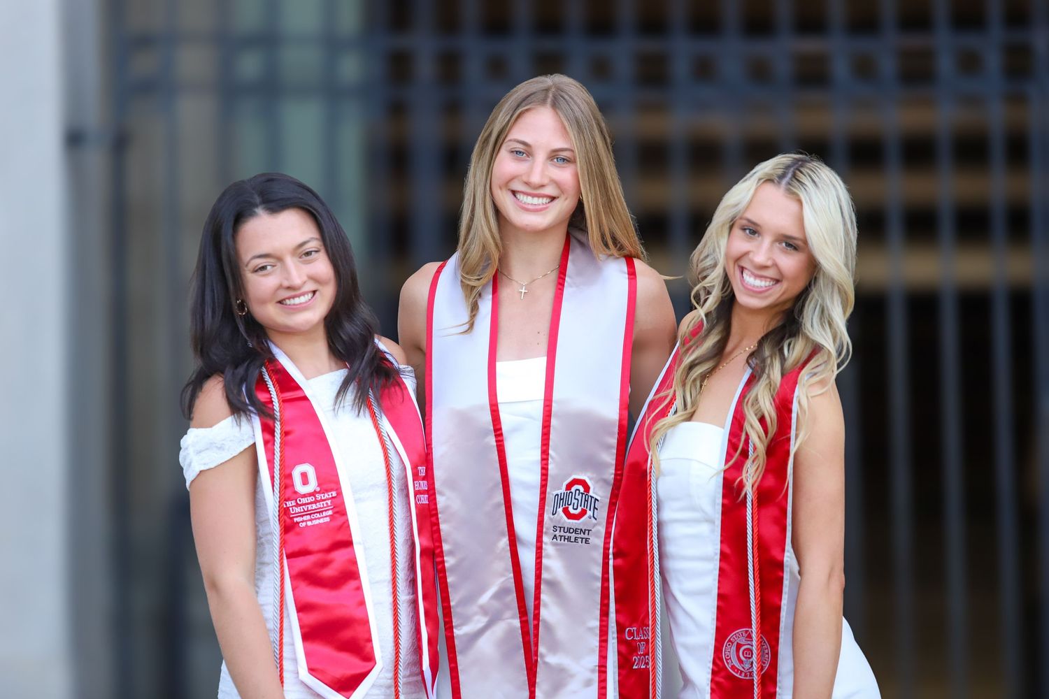 A group of graduates wearing red and white stoles smile together during commencement celebrations.