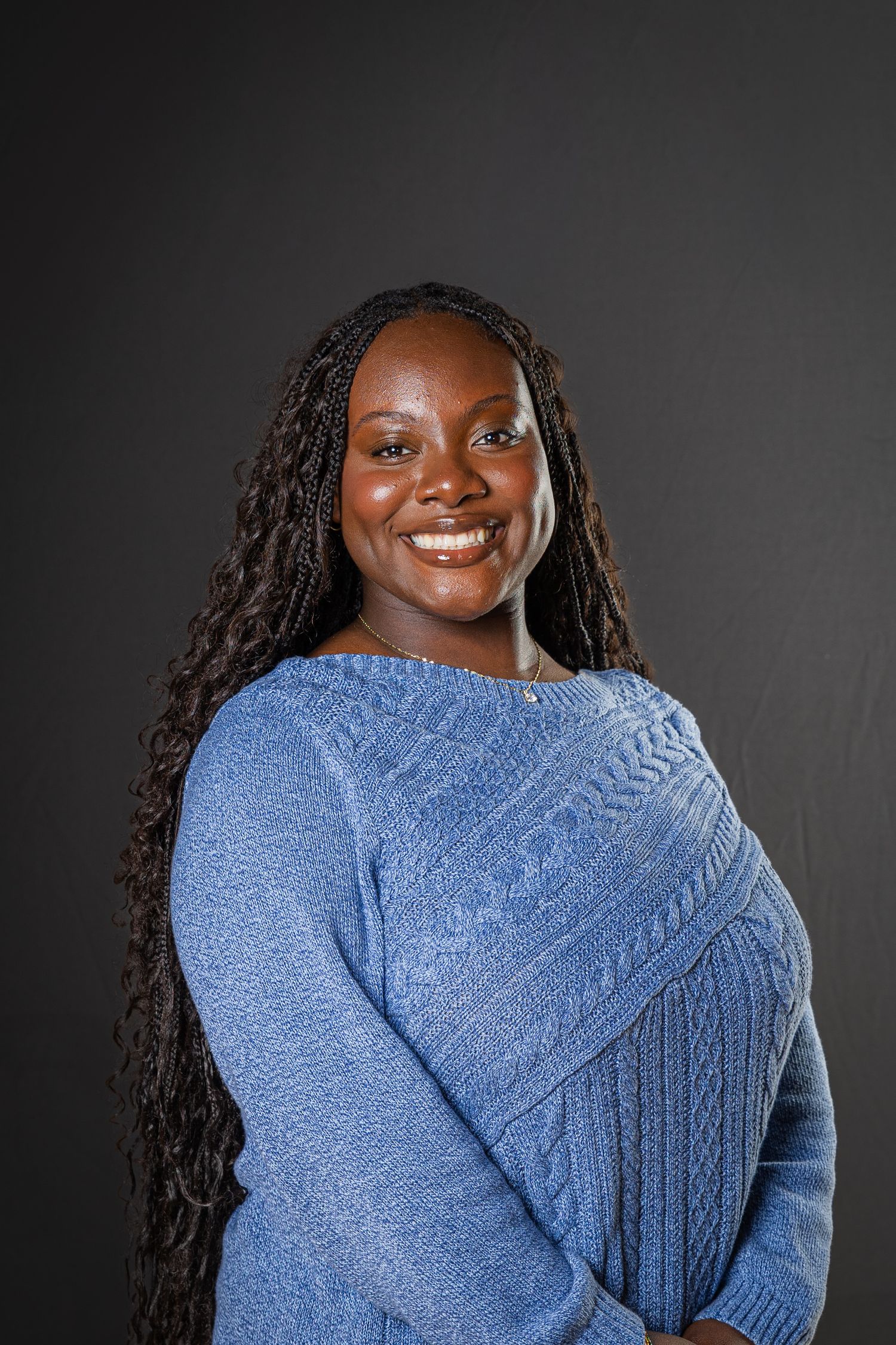 A person in a blue knit sweater poses against a dark background while smiling warmly.