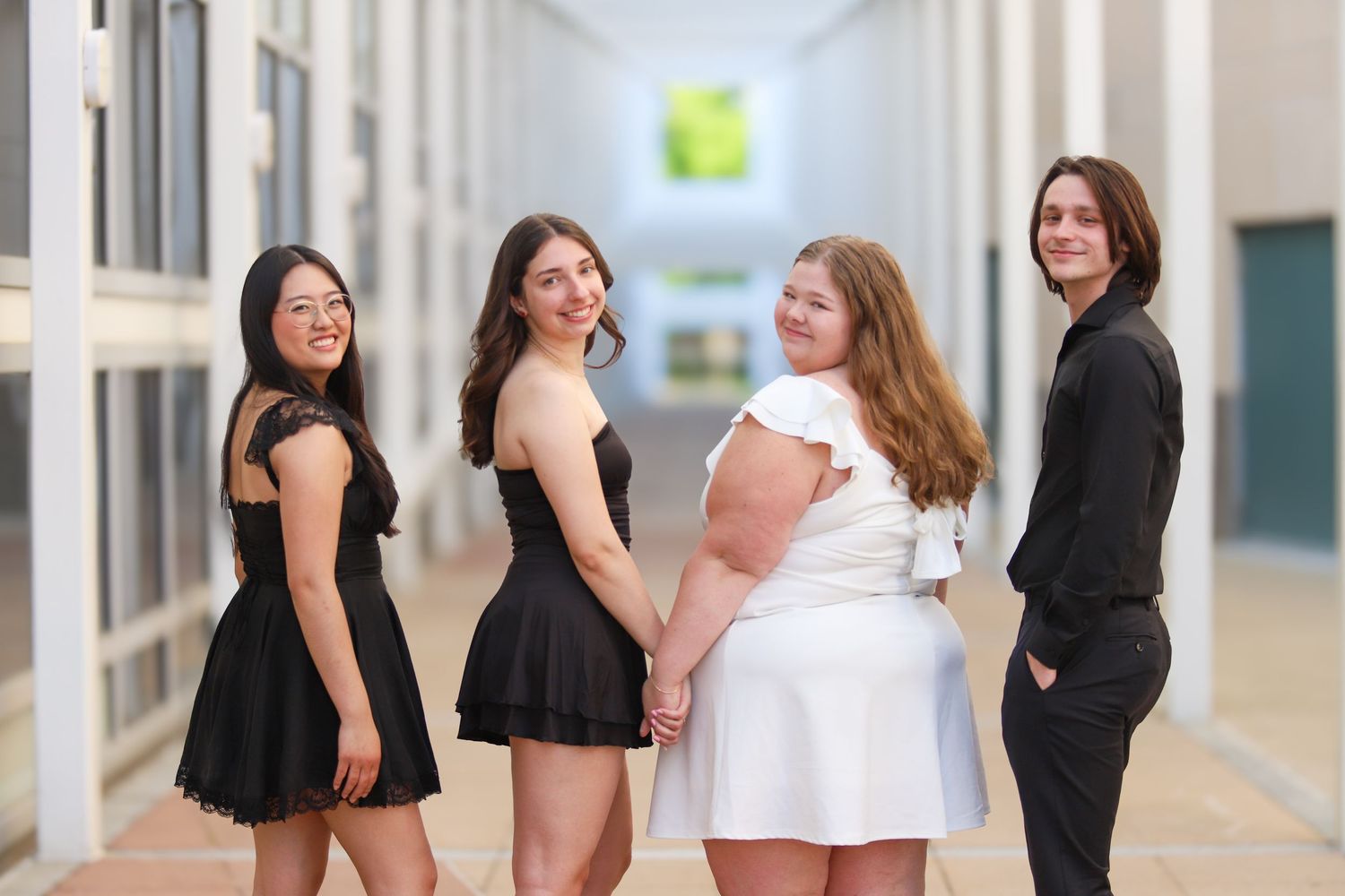 Four students in formal attire pose together in a bright school hallway.