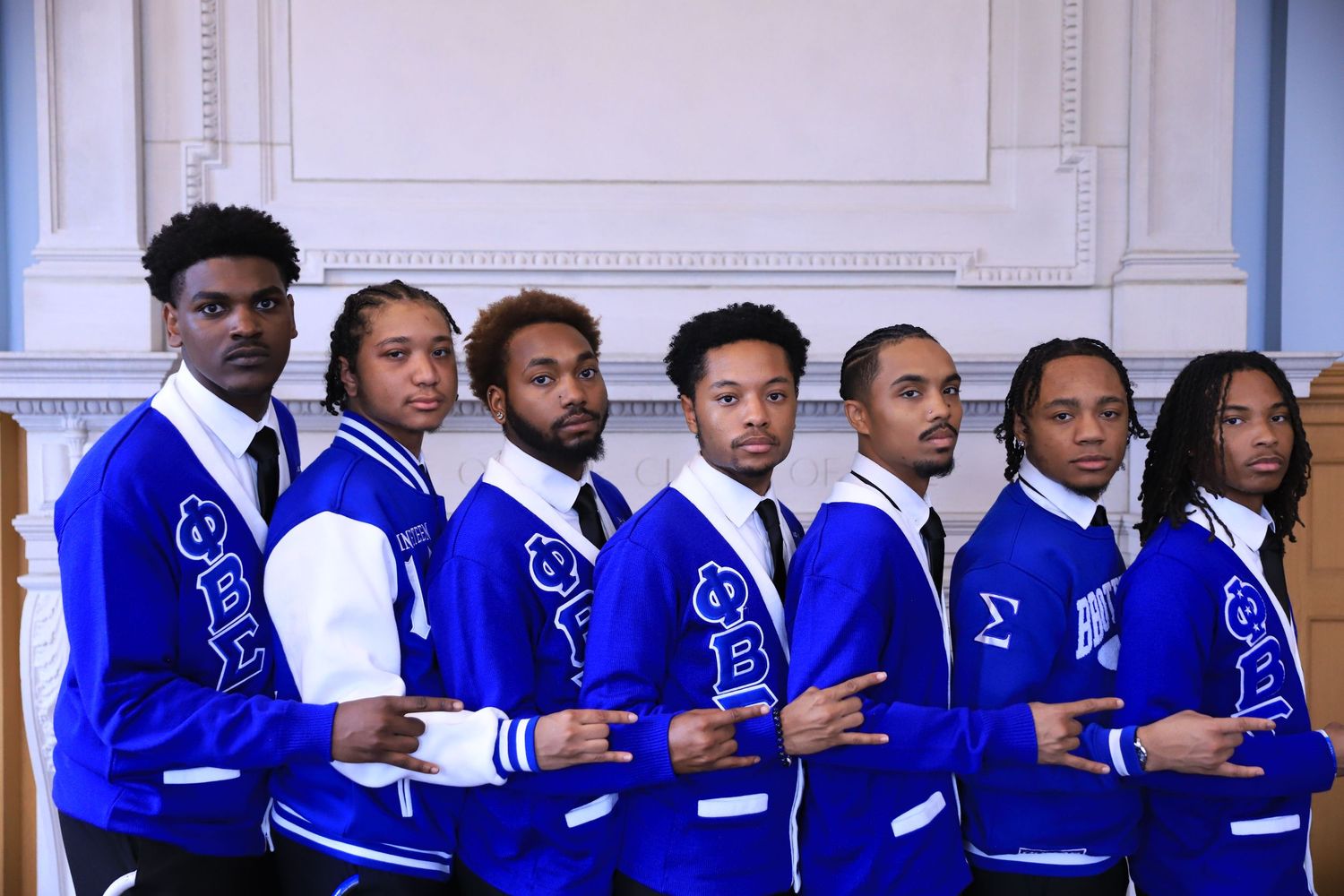 A row of people wearing bright royal blue and white jackets stand together in a formal group setting.