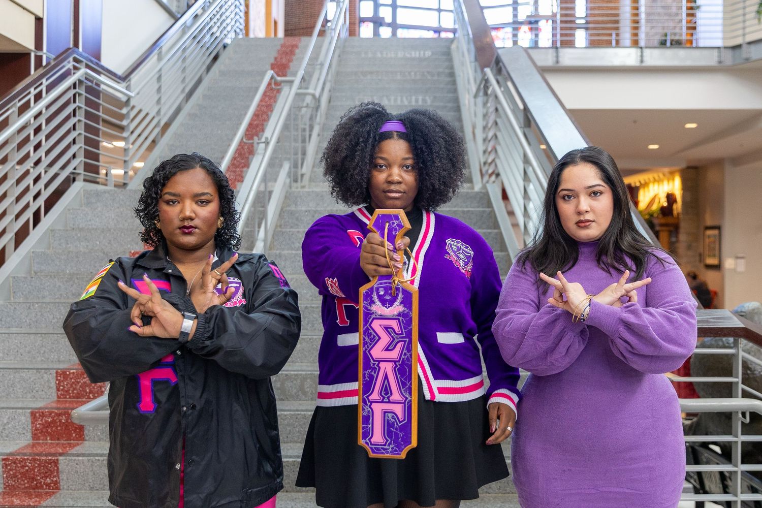 Students wearing purple and black apparel pose together in a hallway holding up letters and signs.