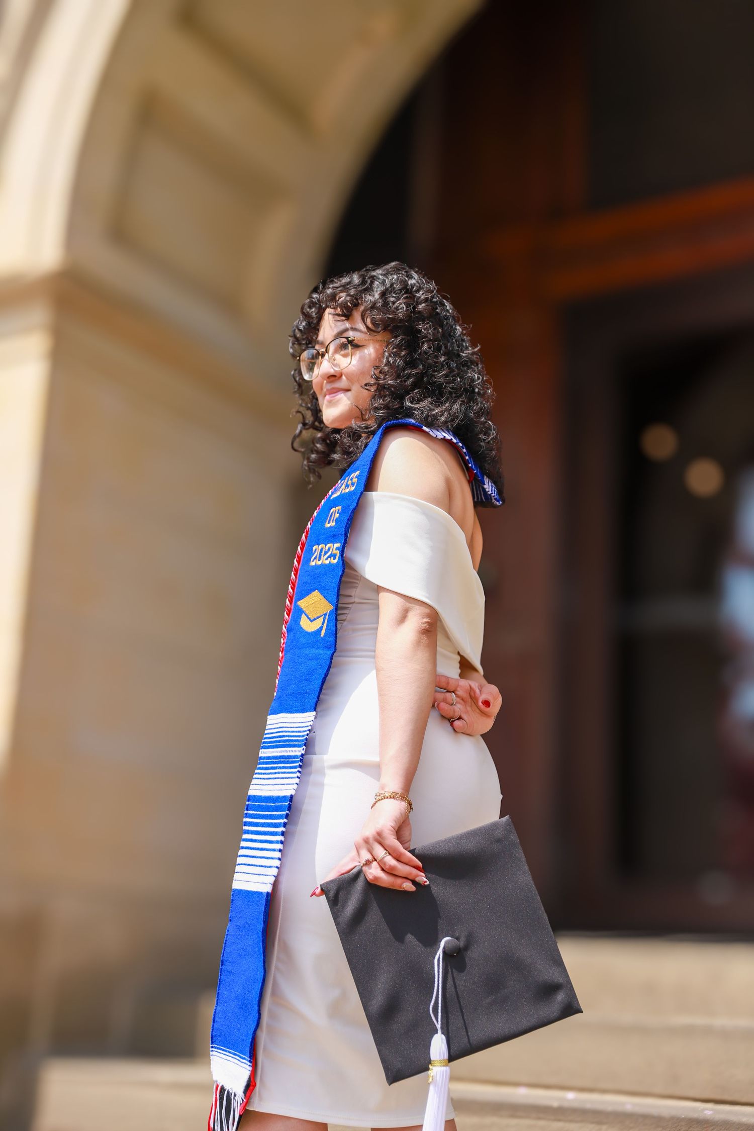 A graduate in white dress and blue graduation stole embraces someone in a tender moment during commencement.