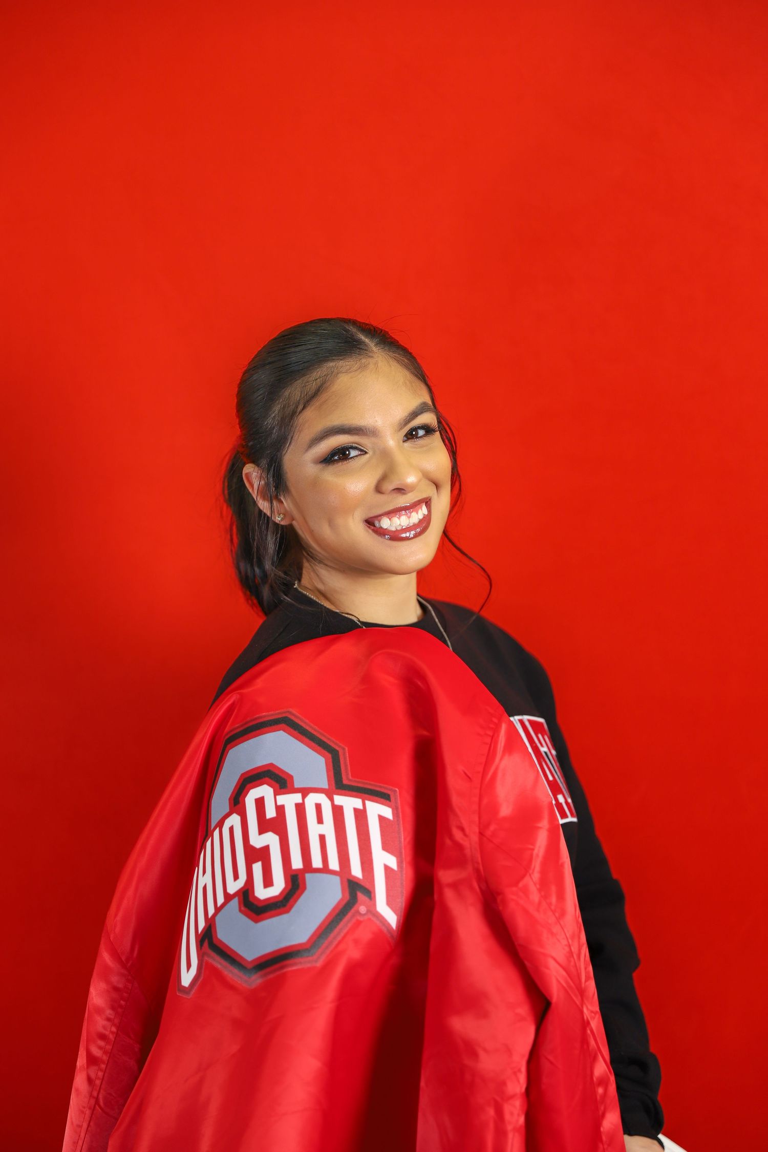 Graduate in red Ohio State jacket poses against vibrant red background showing school spirit.