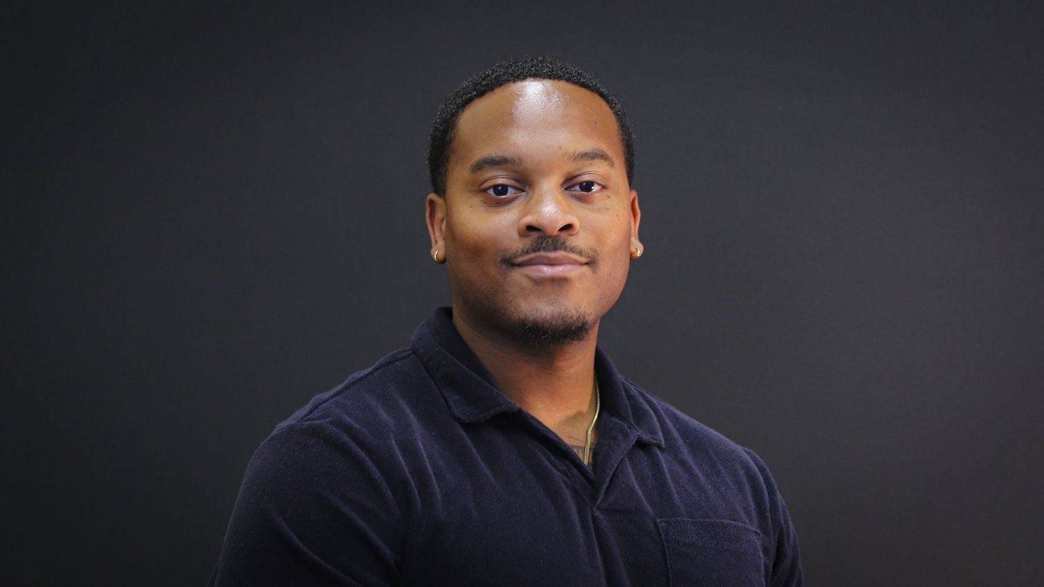 Professional headshot portrait against dark background wearing navy polo shirt.