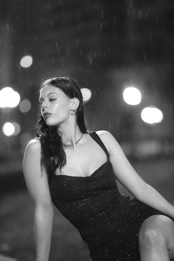A dramatic black and white photo series shows a figure in a dark dress posing expressively against blurred lights.