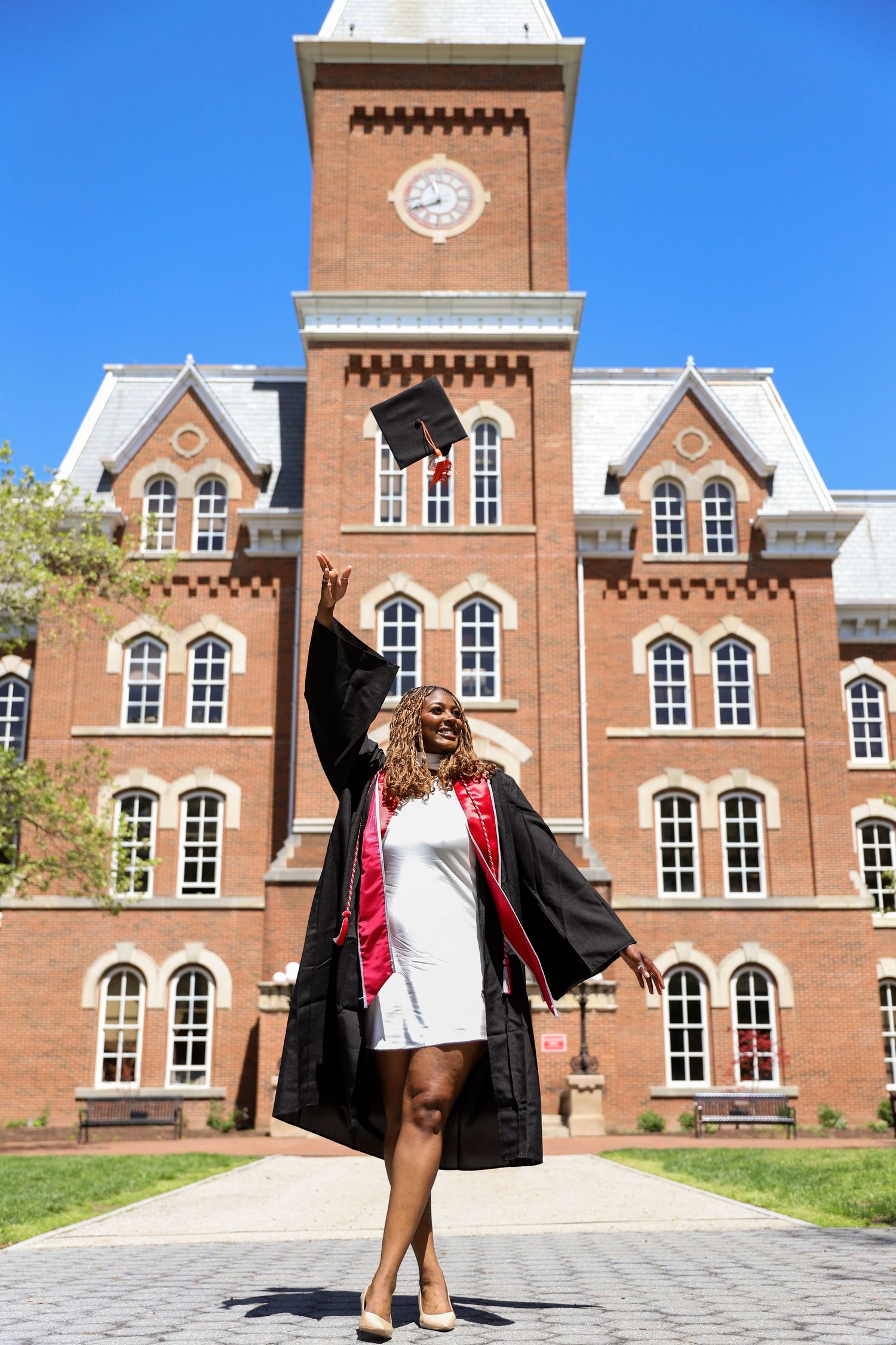 Graduate poses in front of historic brick university building with arched windows.