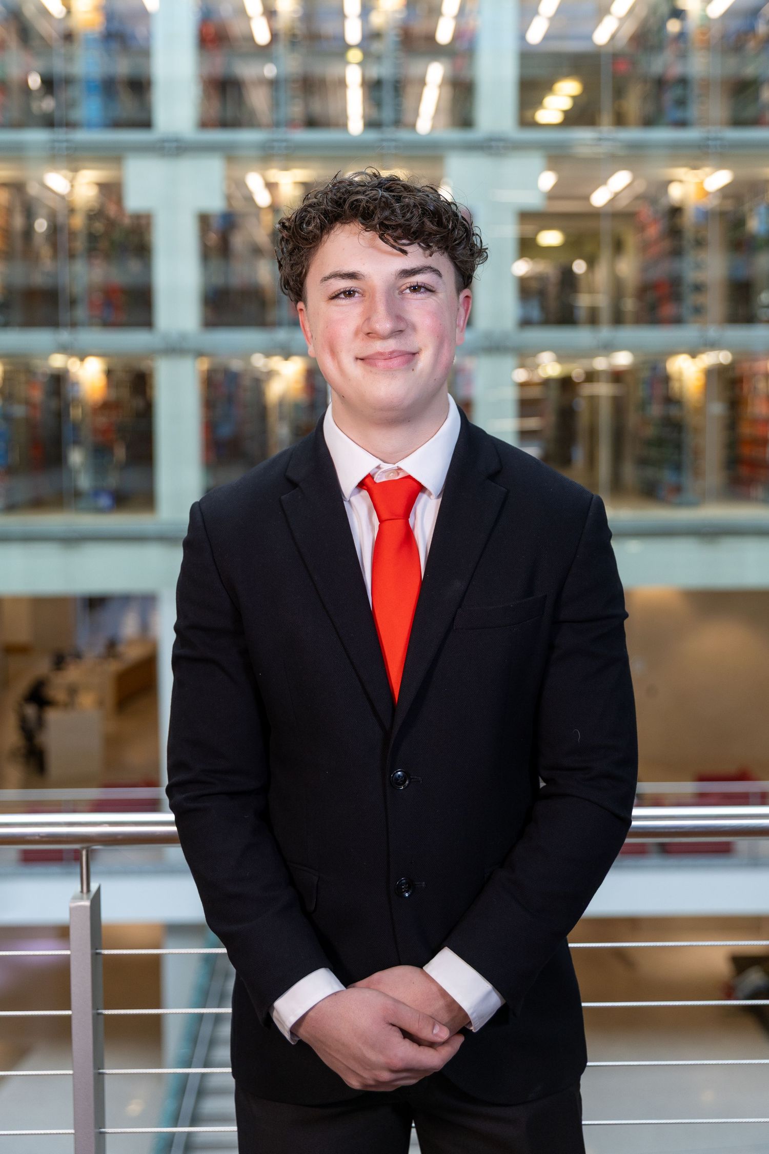 Professional portrait in a black suit and red tie standing in front of a bright indoor commercial space.