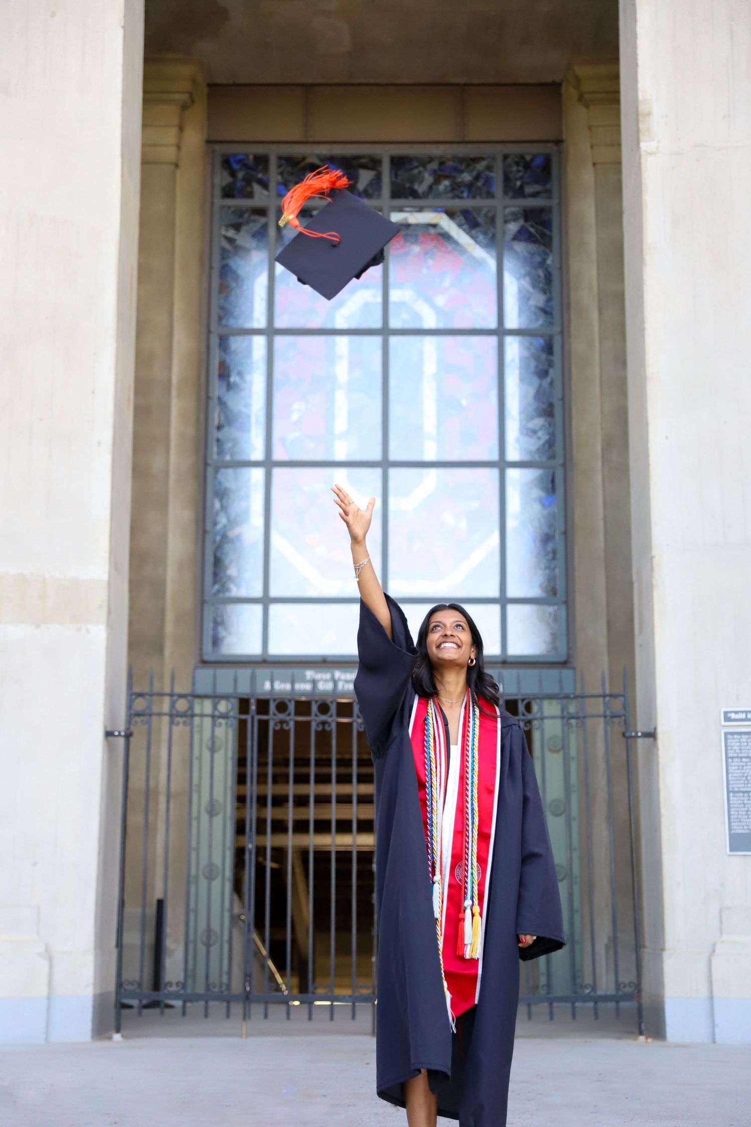 Graduate in cap and gown tosses graduation cap in celebratory poses.