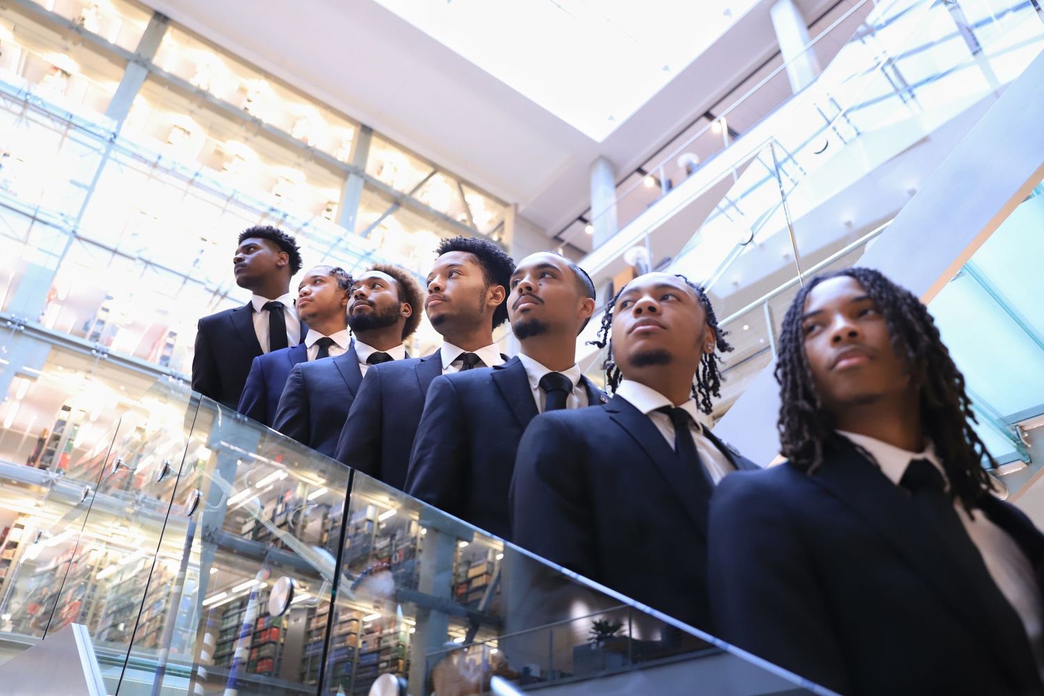 A group of business professionals look up at something off-camera while standing in a modern office building atrium.
