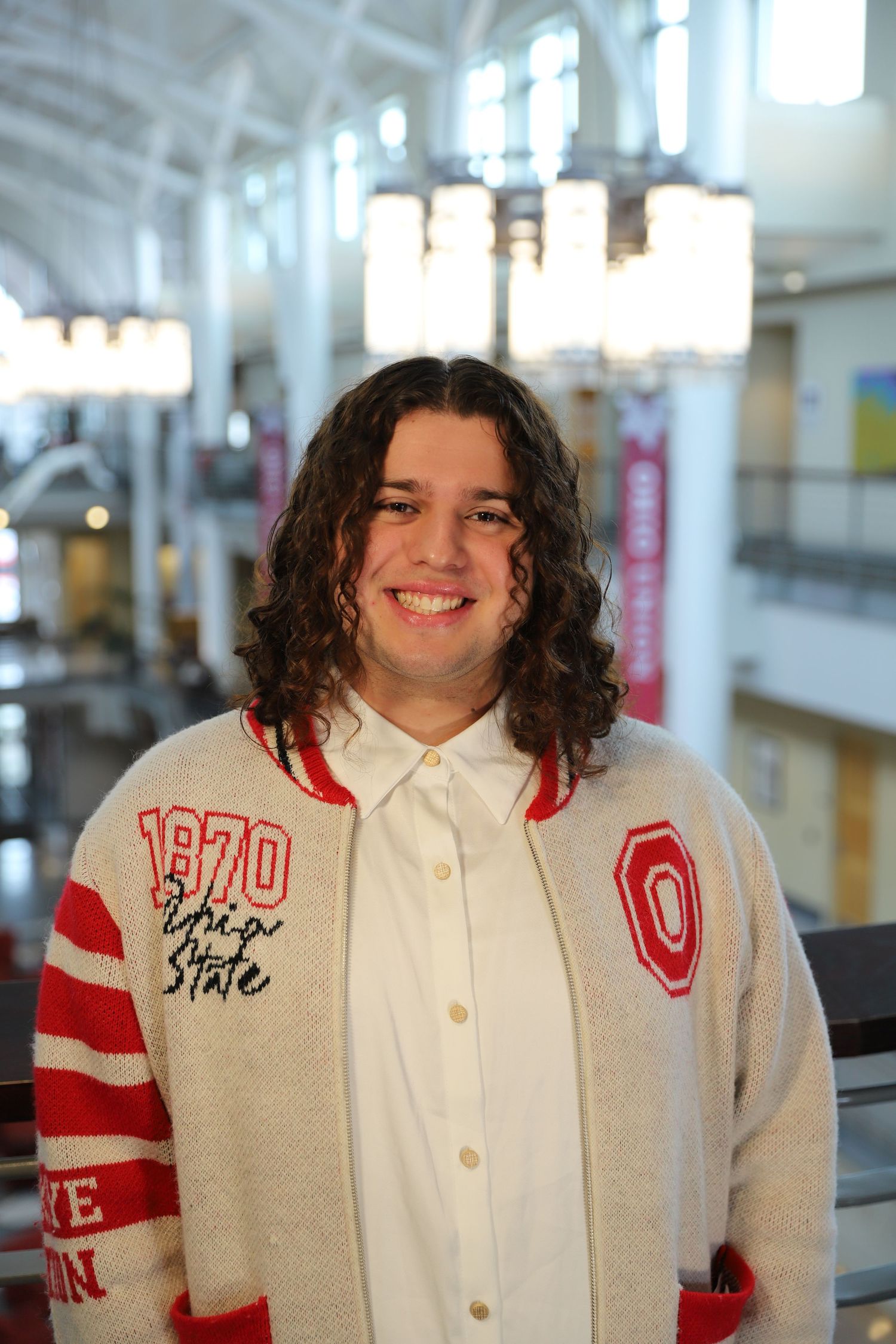 Person wearing a white and red Ohio State varsity style jacket in what appears to be a school hallway.