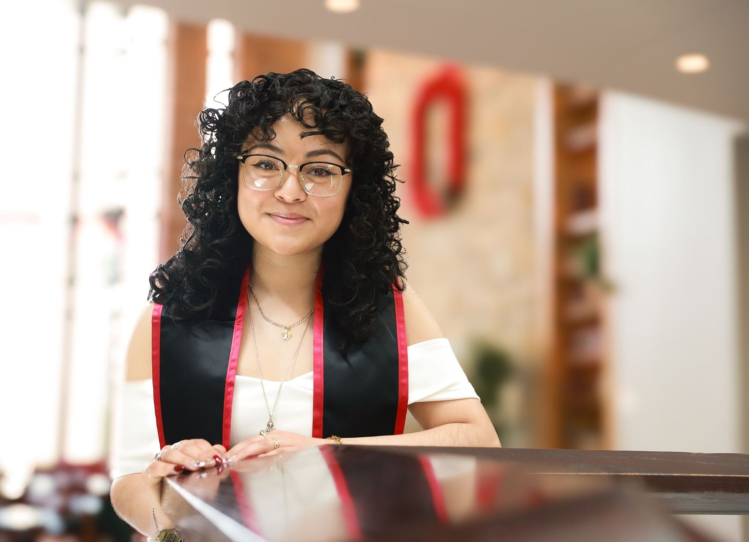 Graduate in glasses poses with diploma in indoor setting.