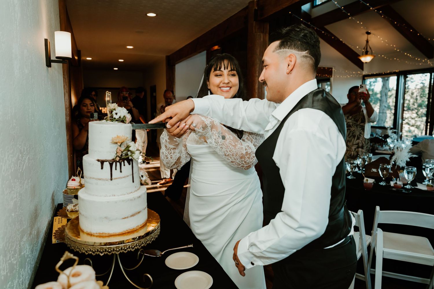 Bride and groom smiling while cutting their elegant wedding cake at a reception venue.