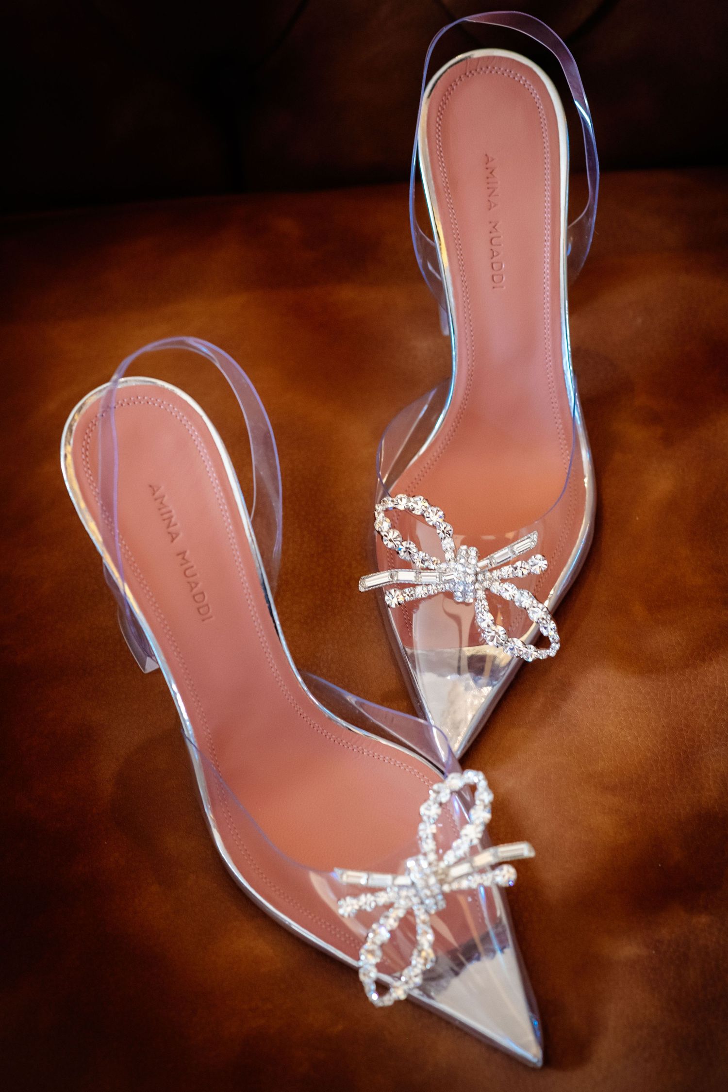 Crystal-embellished clear wedding heels with bow details photographed against warm background.