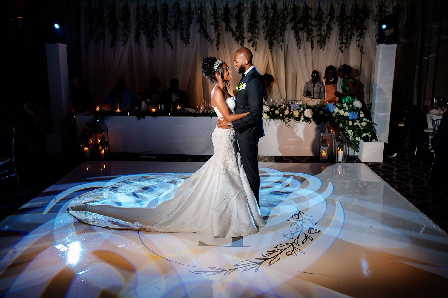 A couple shares their first dance on an illuminated white dance floor at an elegant wedding reception.