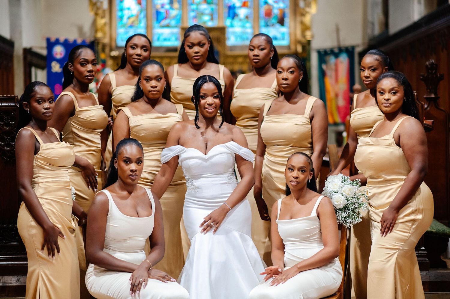 Bridal party in gold and white dresses poses together in church setting.