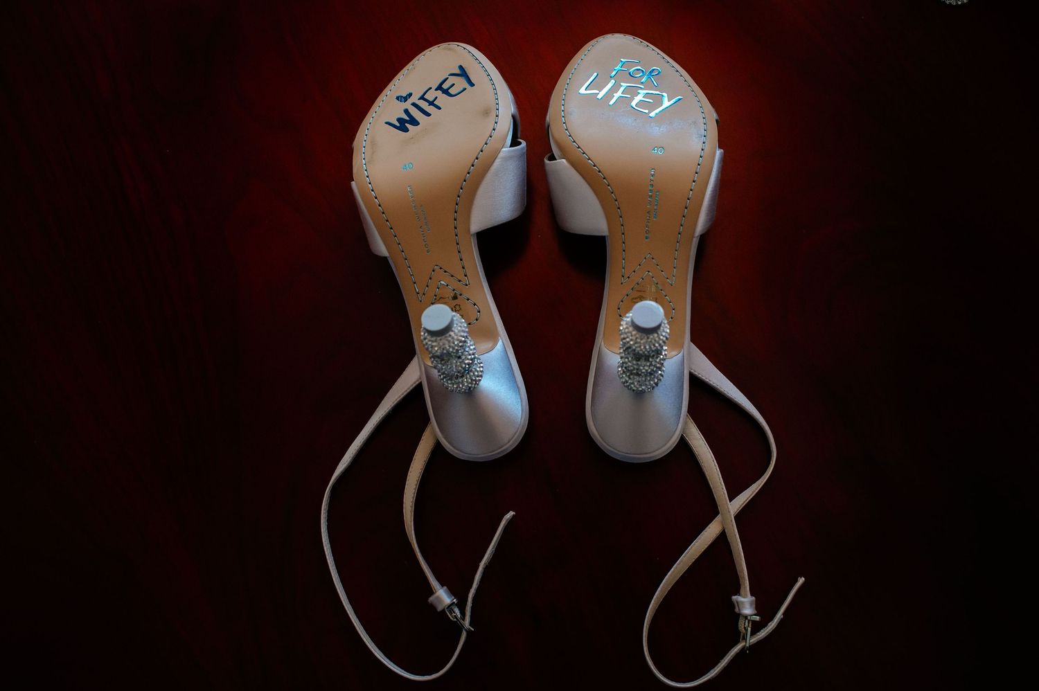 Wedding shoes arranged artistically against dark backdrop showing personalized details.
