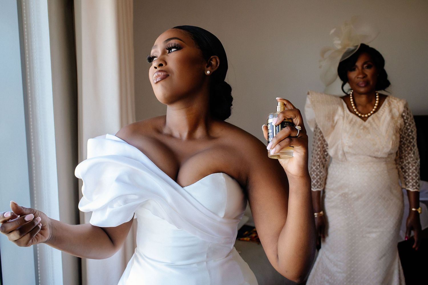 Wedding party getting ready in elegant white dresses by sunlit window.