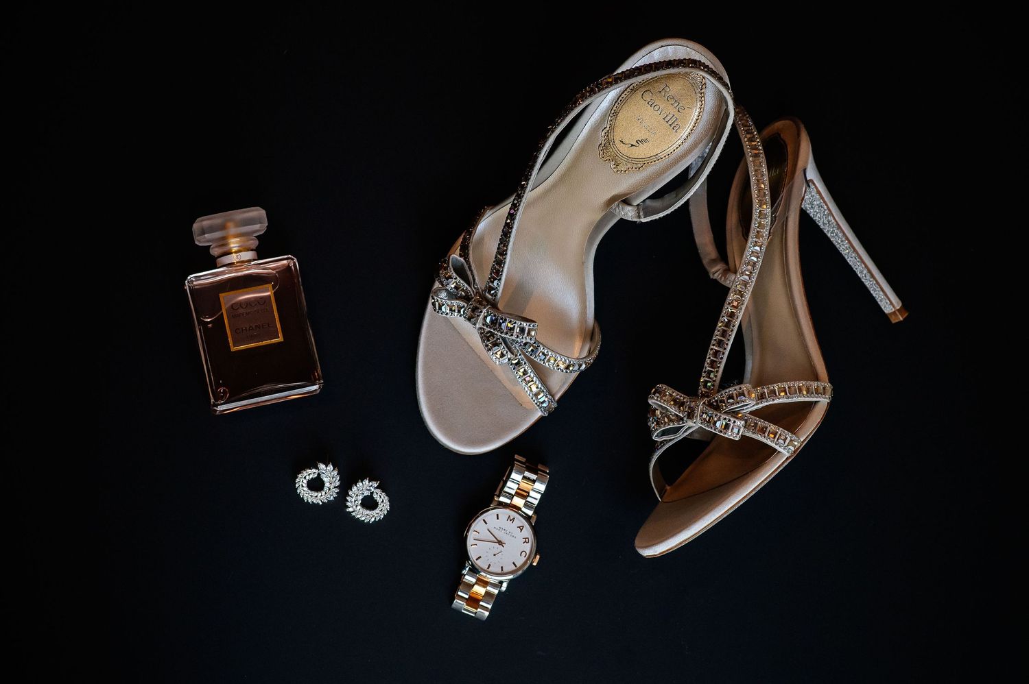 Wedding accessories including perfume bottles, jewelry, and elegant high heels arranged on dark background.