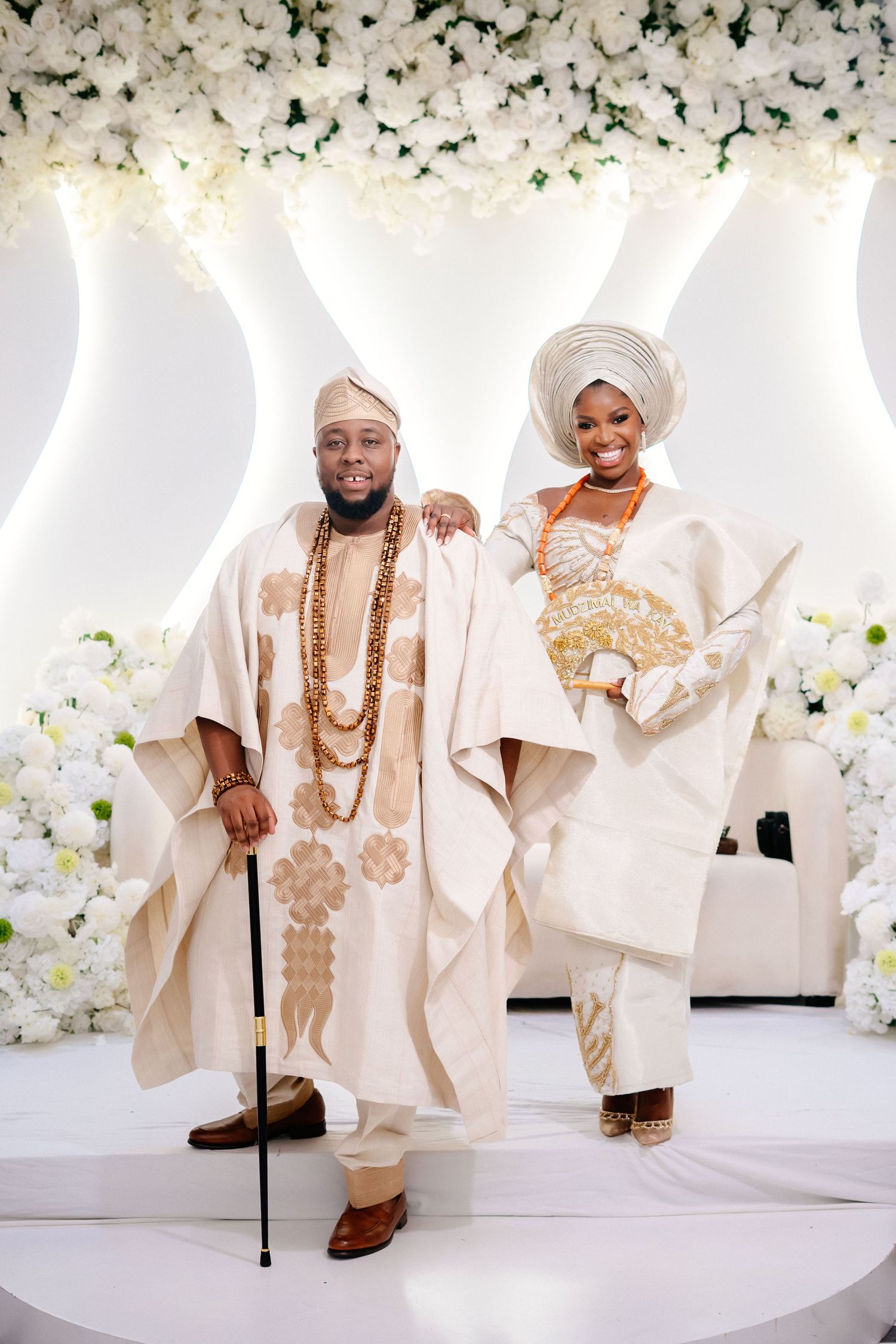 Traditional Nigerian wedding attire displayed in cream and gold against floral backdrop.