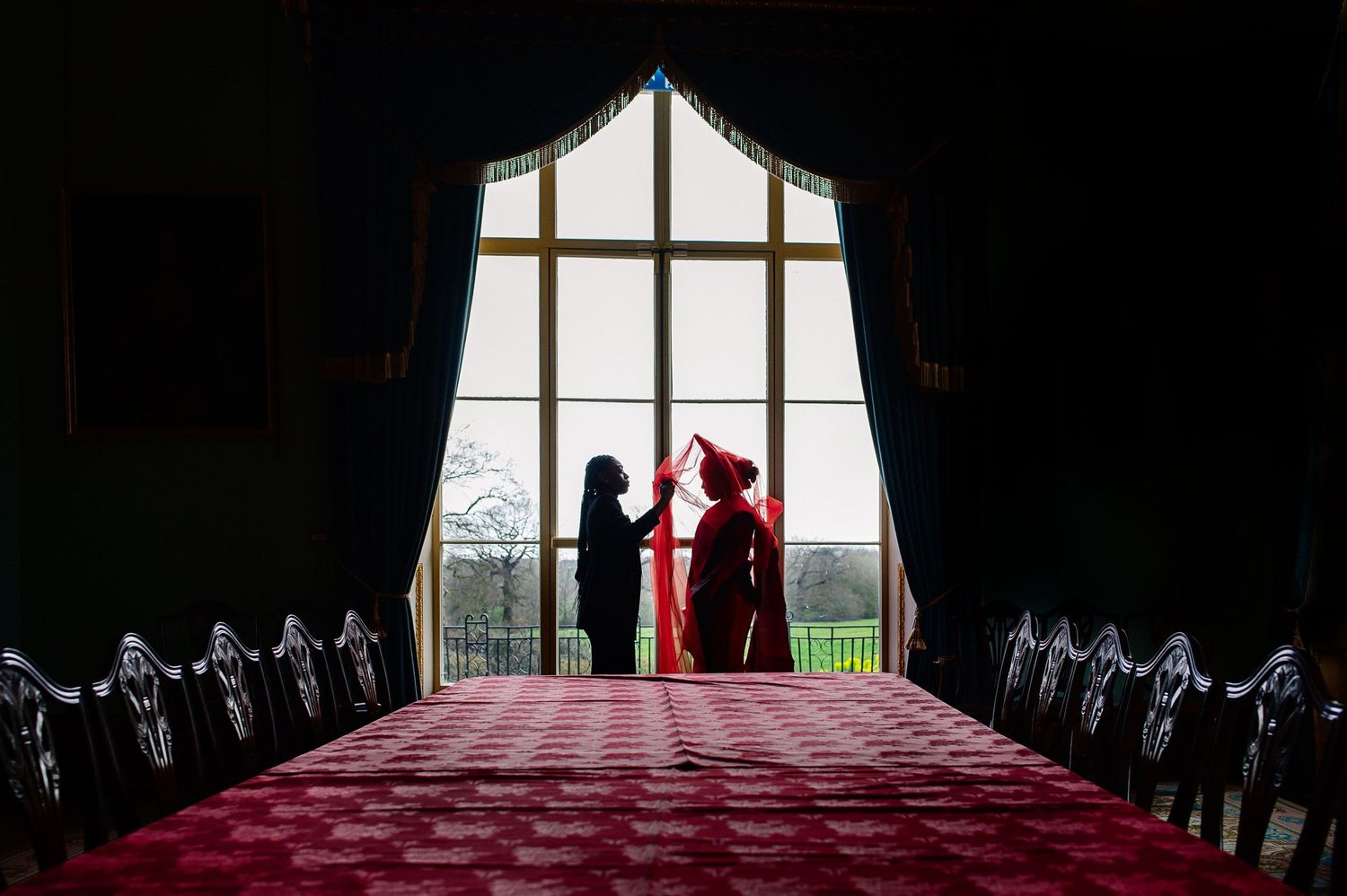 Silhouetted figures by large window in dramatic wedding venue lighting.