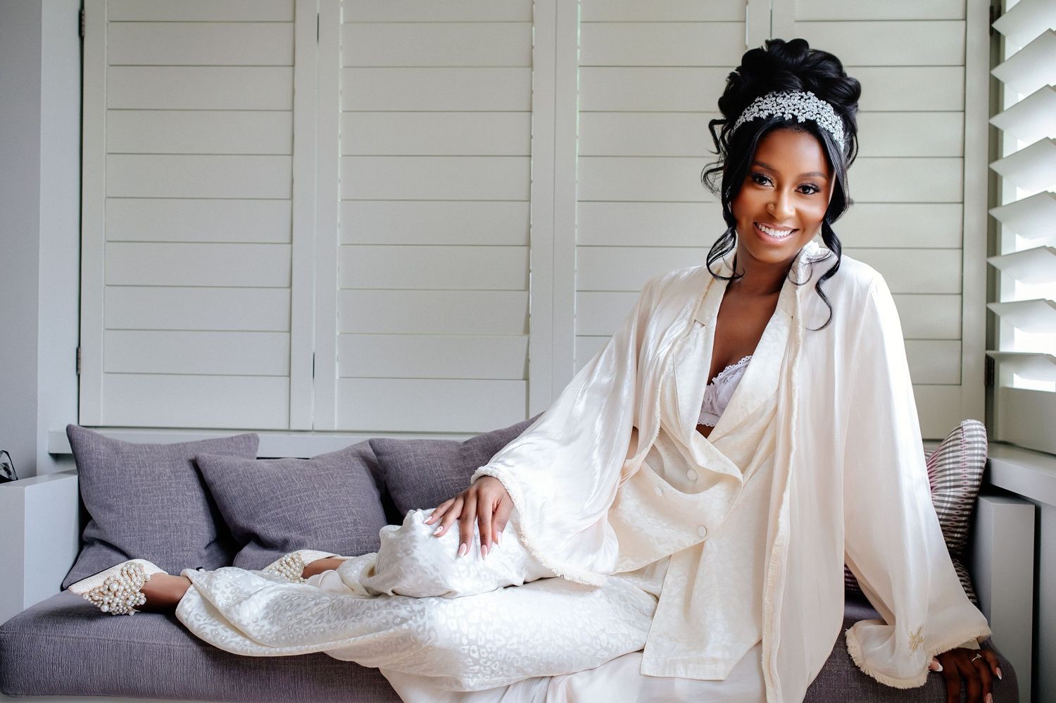 An elegant bridal morning portrait on a grey sofa with white silk robes.