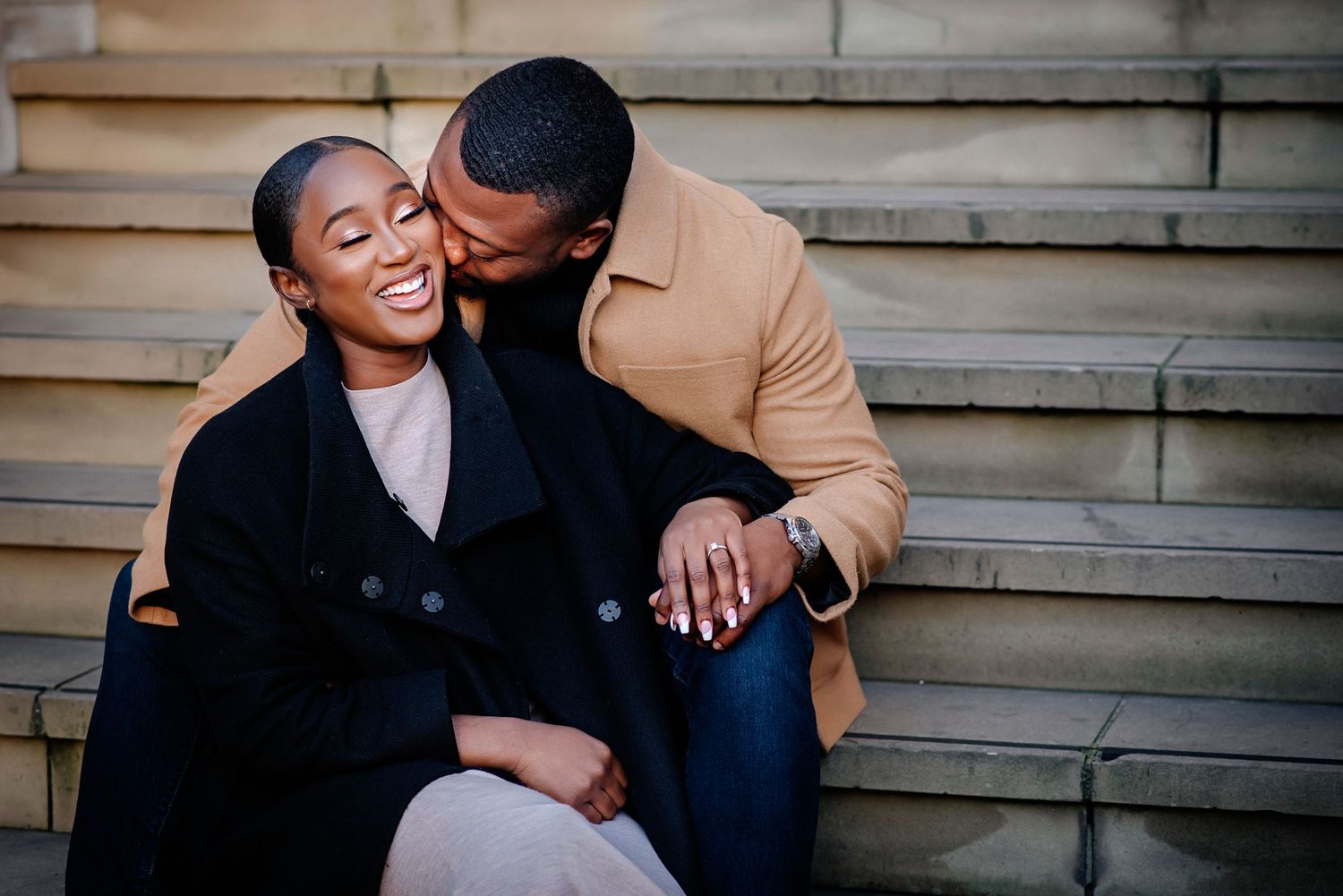 A couple shares joyful moments together while sitting on wooden steps outdoors.