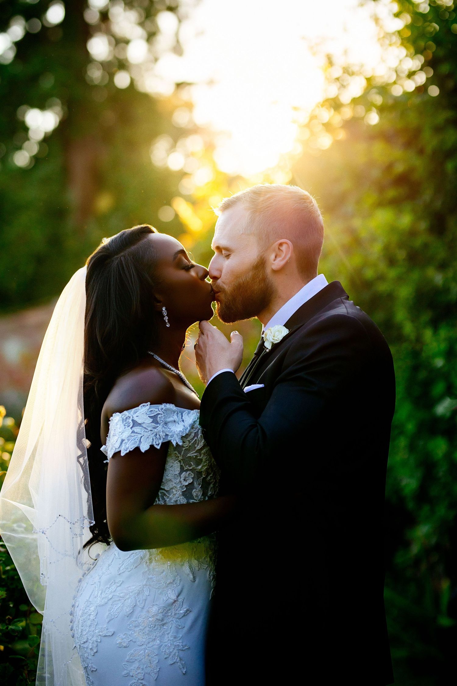 Romantic sunset portrait of newlyweds sharing tender moment among garden greenery.