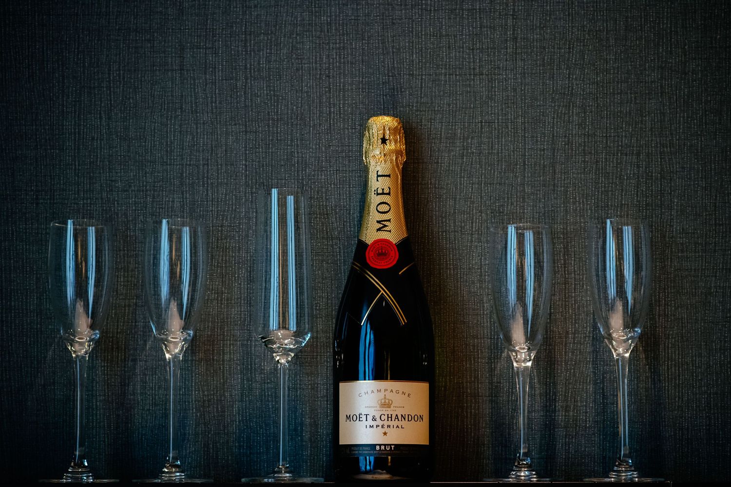 A row of empty champagne flutes with a bottle of Moet Chandon on a dark background.