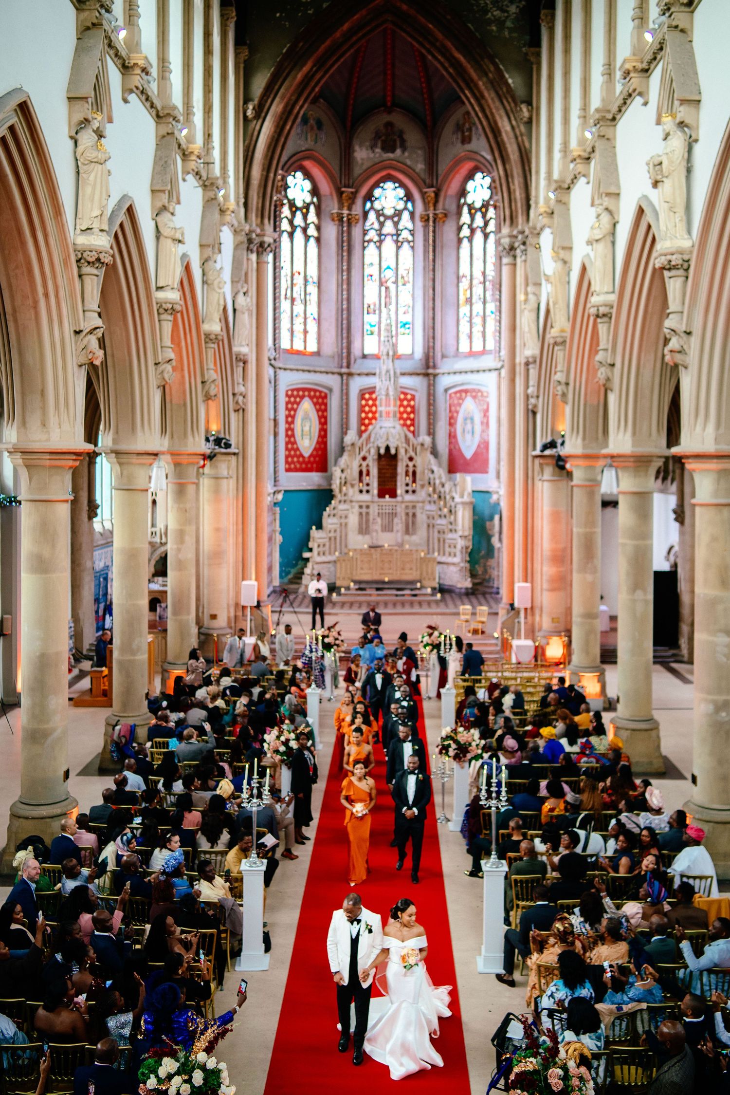 Cathedral wedding ceremony with red carpet aisle and gothic architecture filled with seated guests.