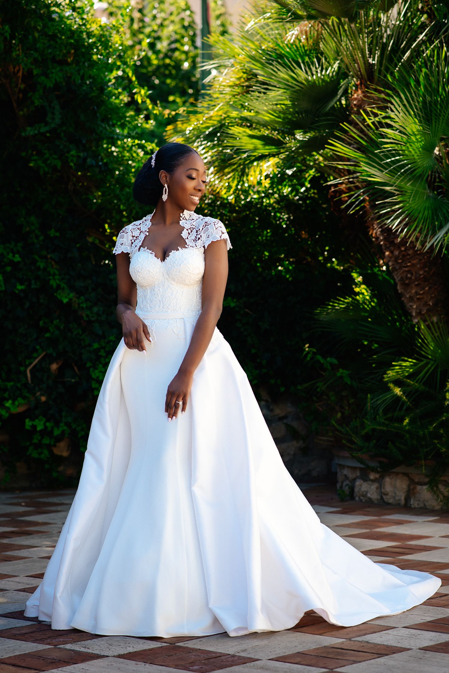 Elegant white wedding gown with lace cap sleeves and long train in tropical garden setting.