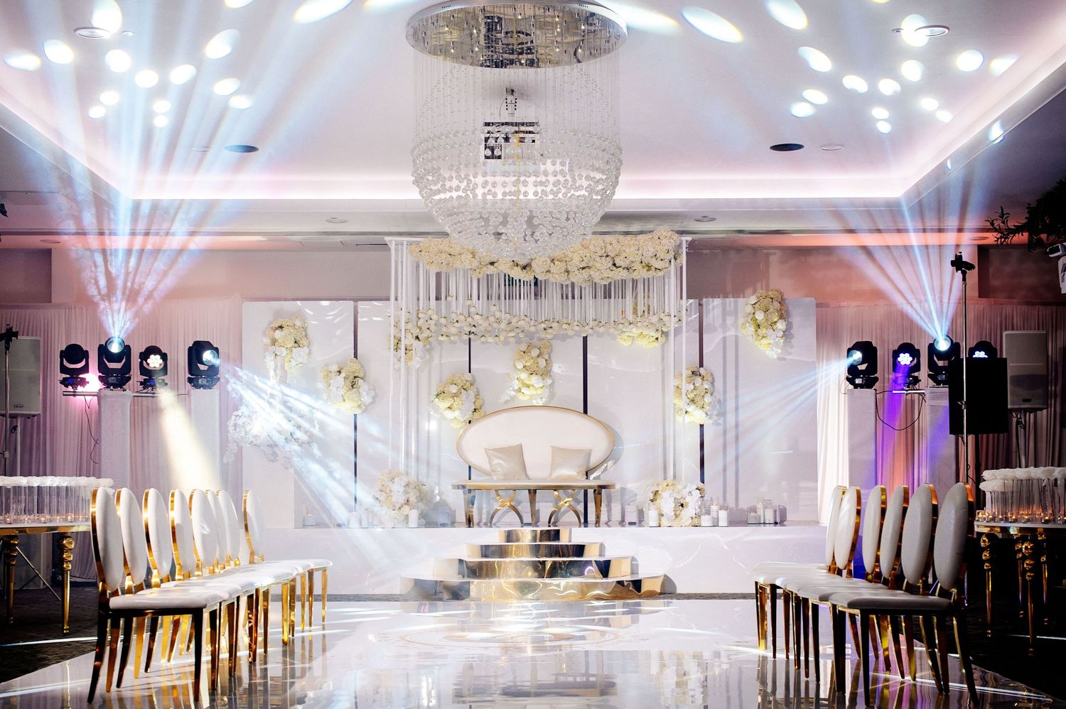 Elegant white banquet hall with crystal chandeliers, spotlights, and modern decor for luxurious events.
