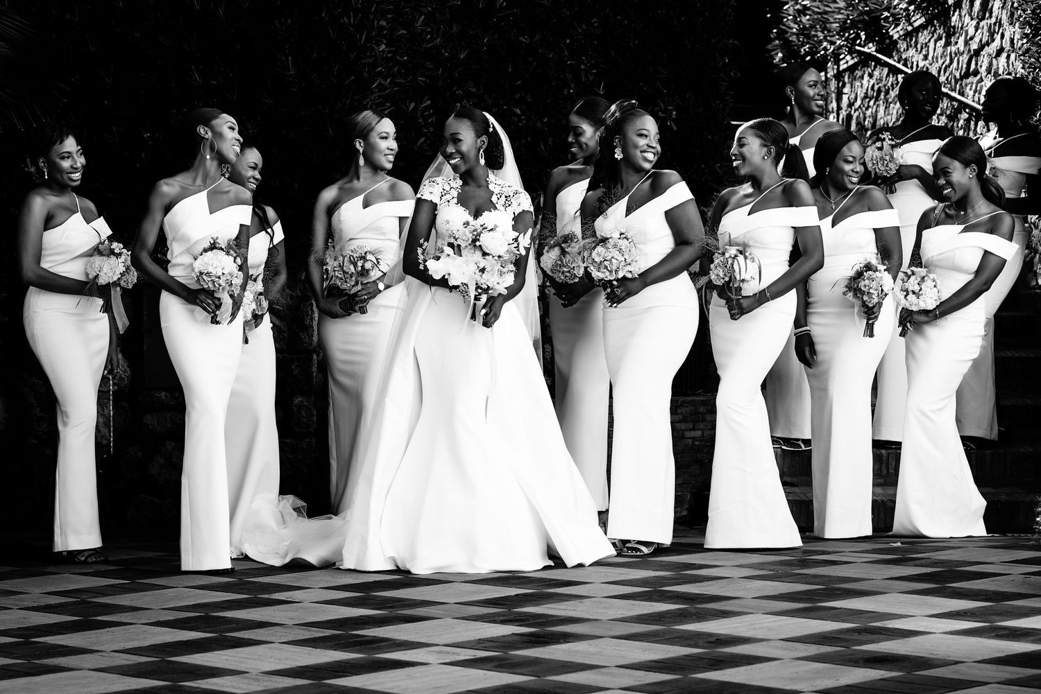 Black and white wedding party lineup shows bridesmaids in elegant dresses standing in formation.