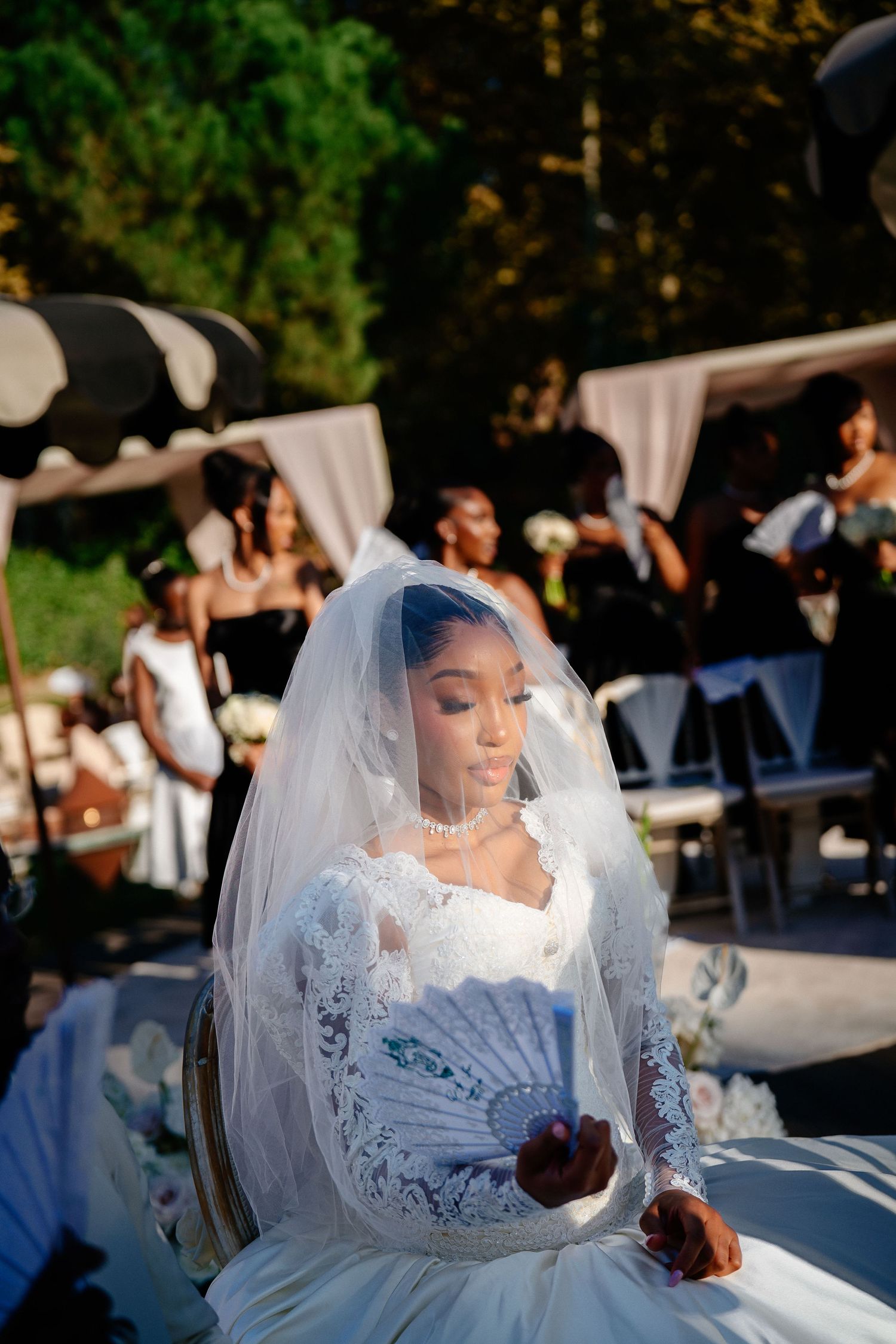 Bride in an elegant white lace dress and veil poses during an outdoor wedding celebration.
