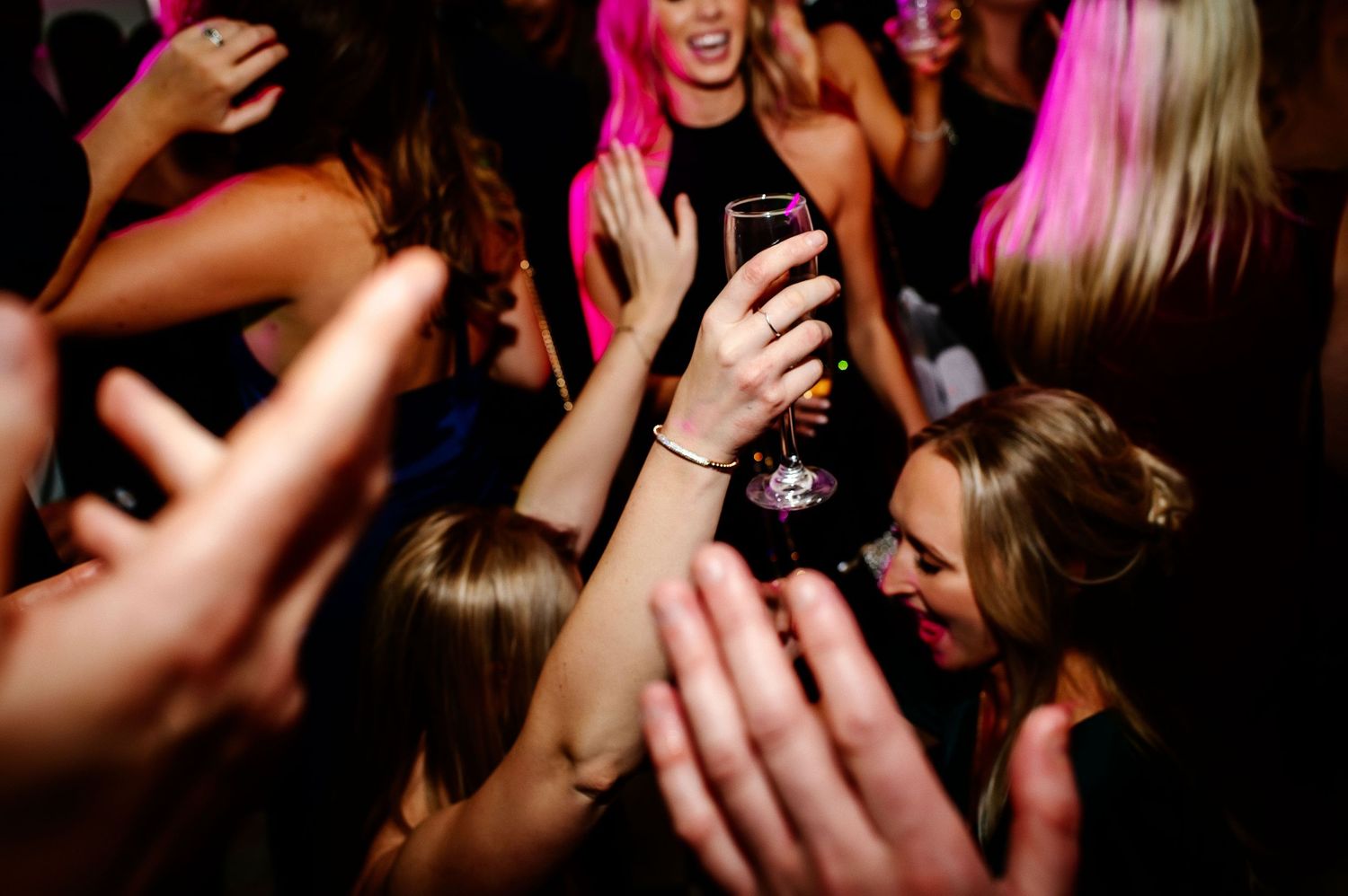 Energetic dance floor scene with hands raised during wedding reception celebration.