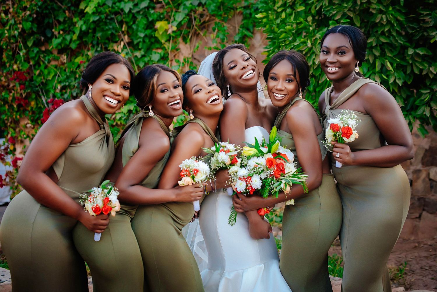 Bridesmaids in olive green dresses pose playfully in a candid photo series against lush garden greenery.