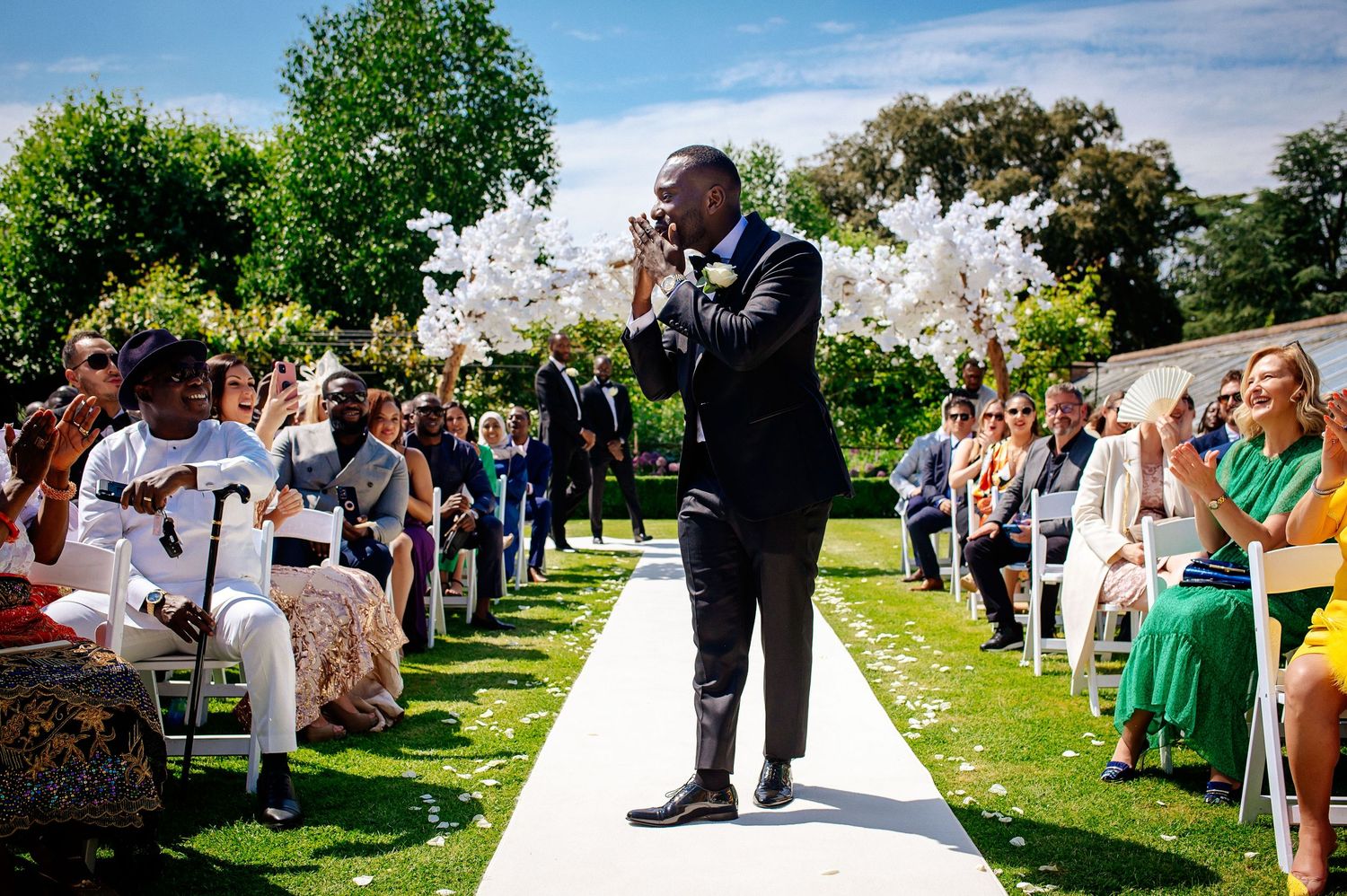 Outdoor garden wedding ceremony with guests seated along tree-lined path.