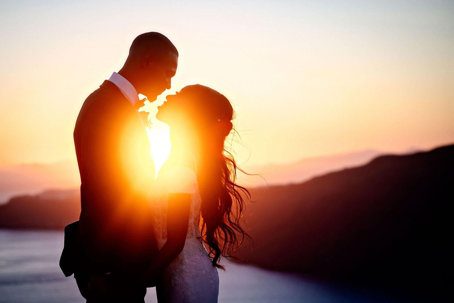 Silhouetted figures stand against a dramatic sunset creating a romantic backlit scene.