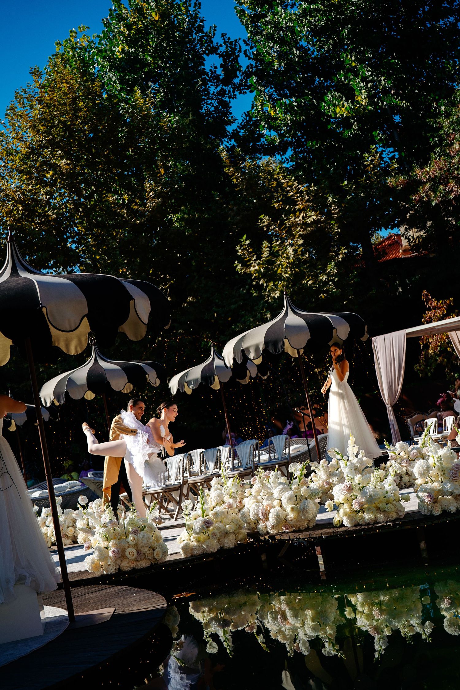 White floral wedding decorations line an outdoor ceremony space under a bright blue sky.