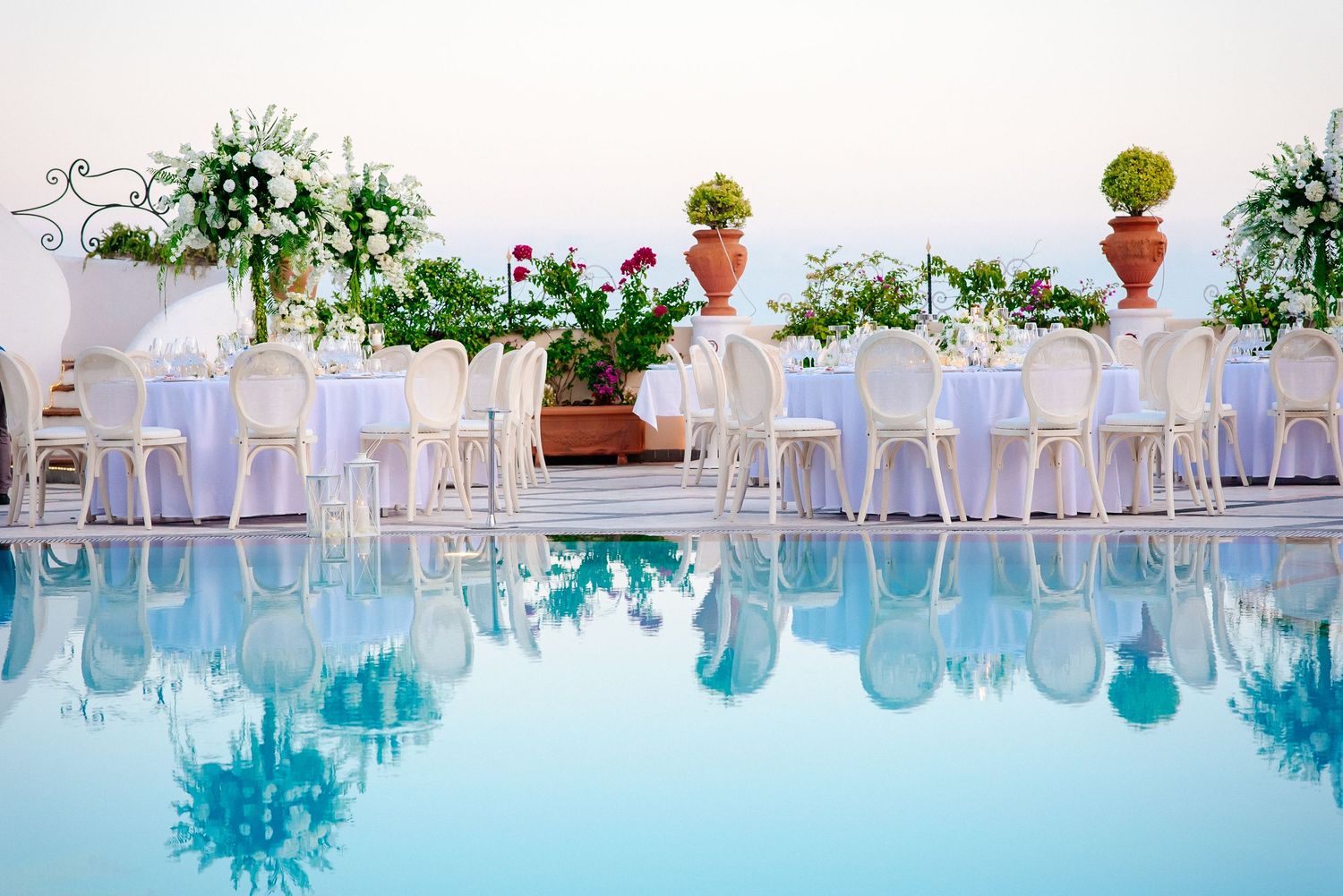 Elegant poolside wedding reception setup with white chairs and floral decorations.