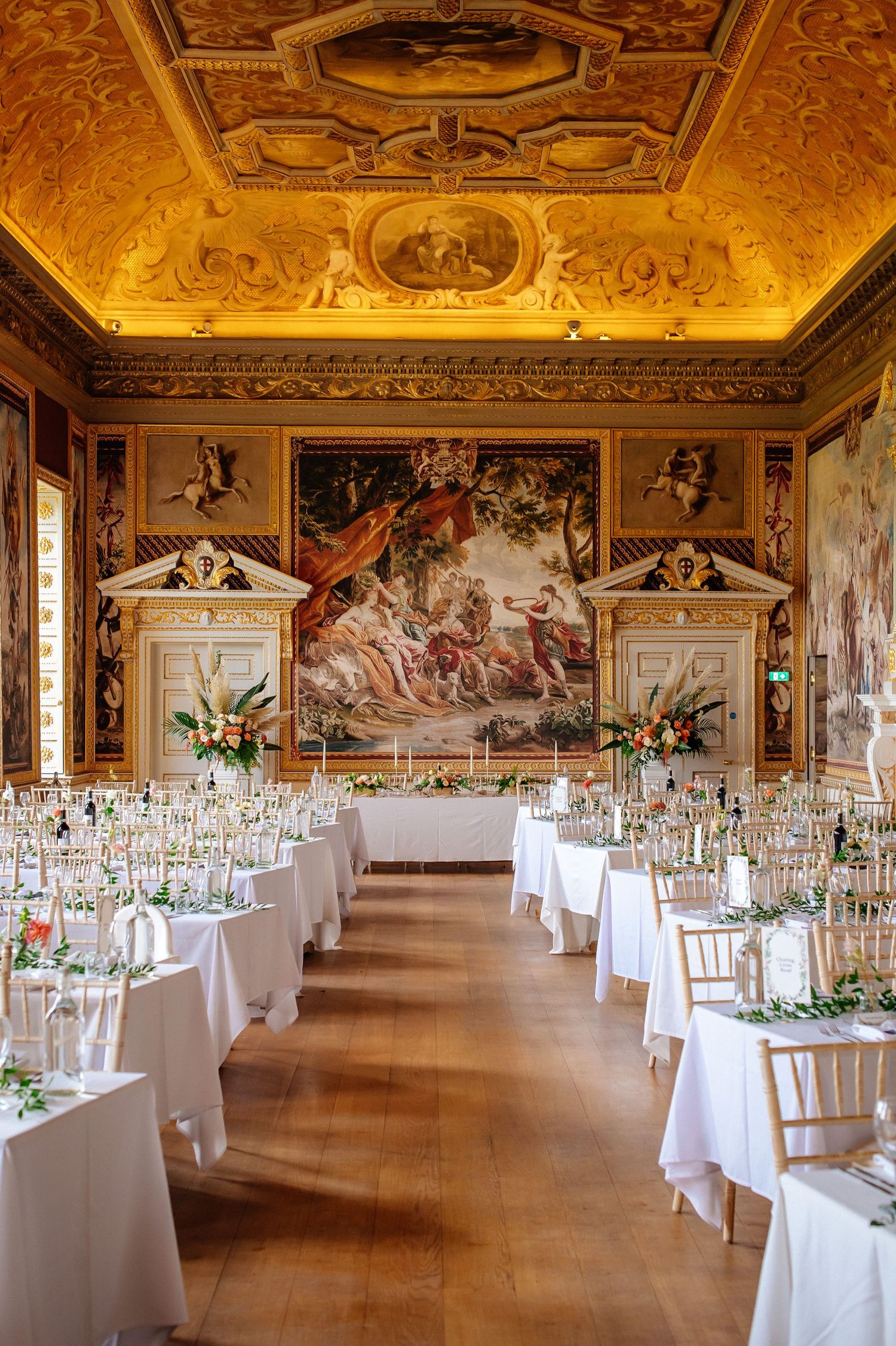 Elegant banquet hall with ornate frescoed ceiling and white-clothed tables set for a formal event in a historic palace.