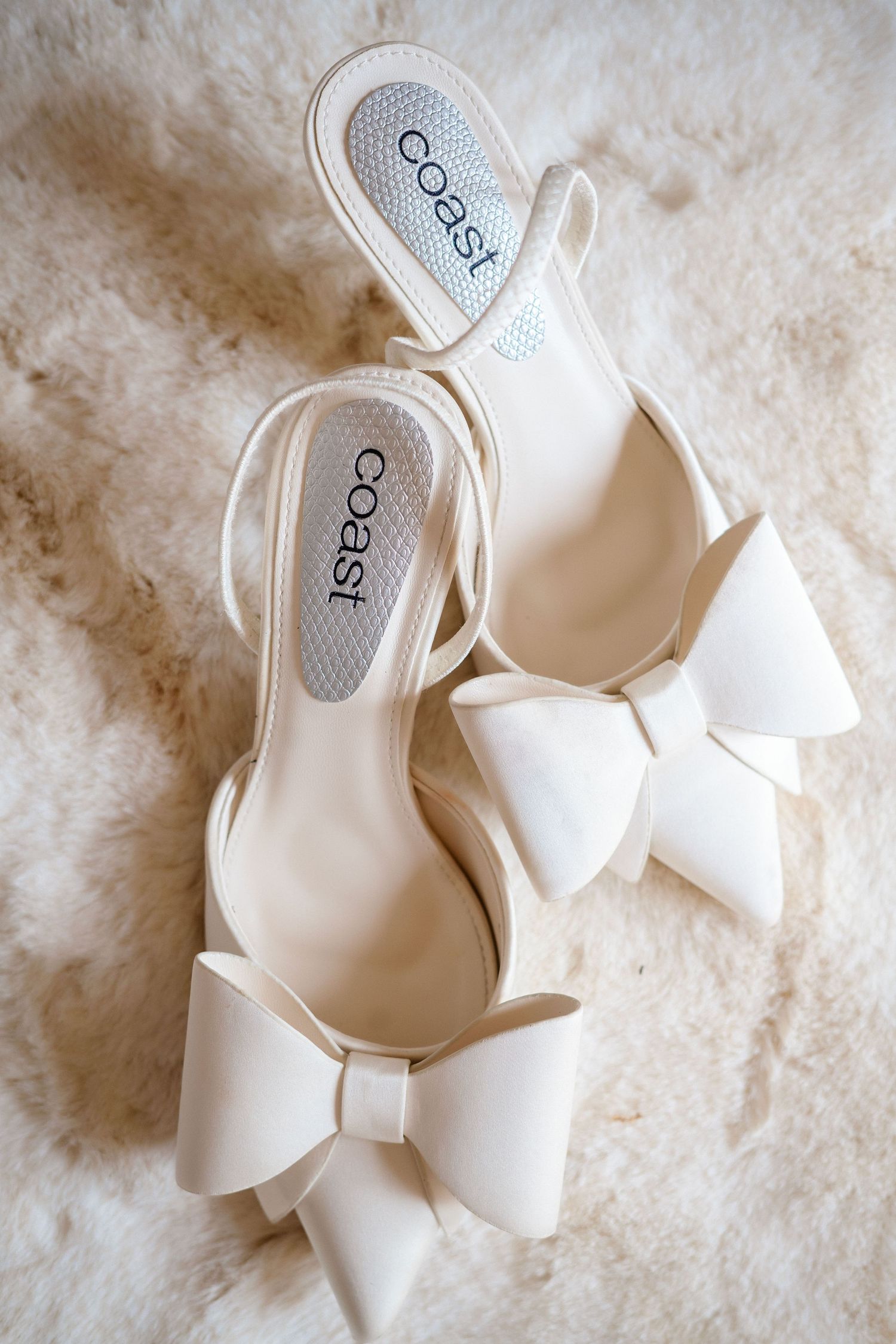 White bridal shoes with elegant bow details photographed on textured background.